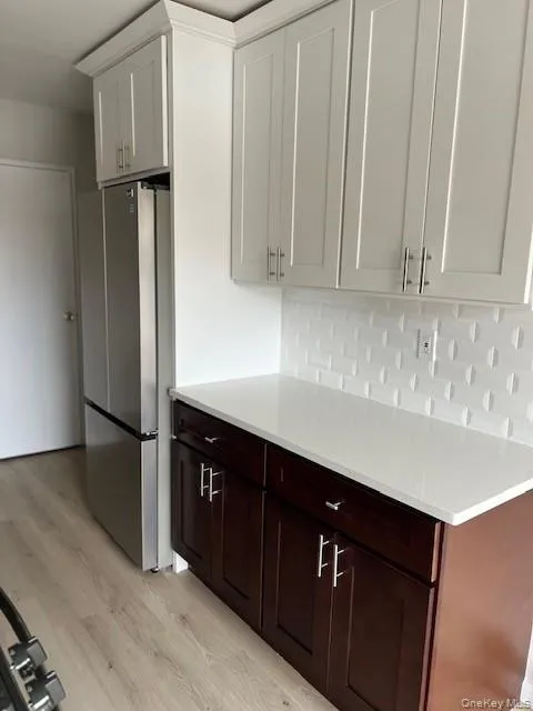 Kitchen featuring freestanding refrigerator, light wood-style flooring, backsplash, light stone counters, and white cabinetry Kitchen featuring freestanding refrigerator, light wood-style flooring, backsplash, light stone counters, and white cabinetry