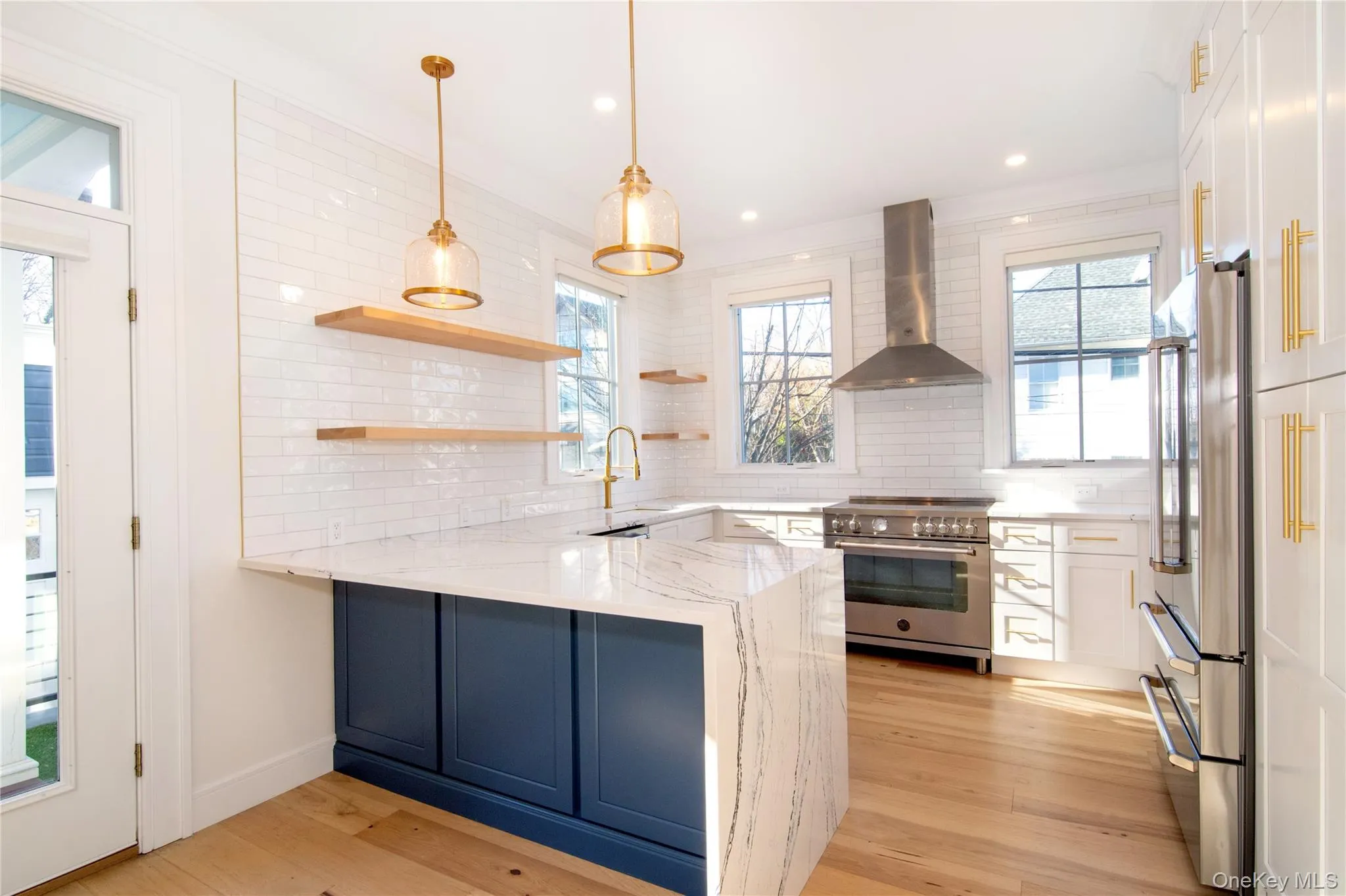 Light filled kitchen featuring a waterfall island, open shelving, and high end stainless steel appliances Light filled kitchen featuring a waterfall island, open shelving, and high end stainless steel appliances