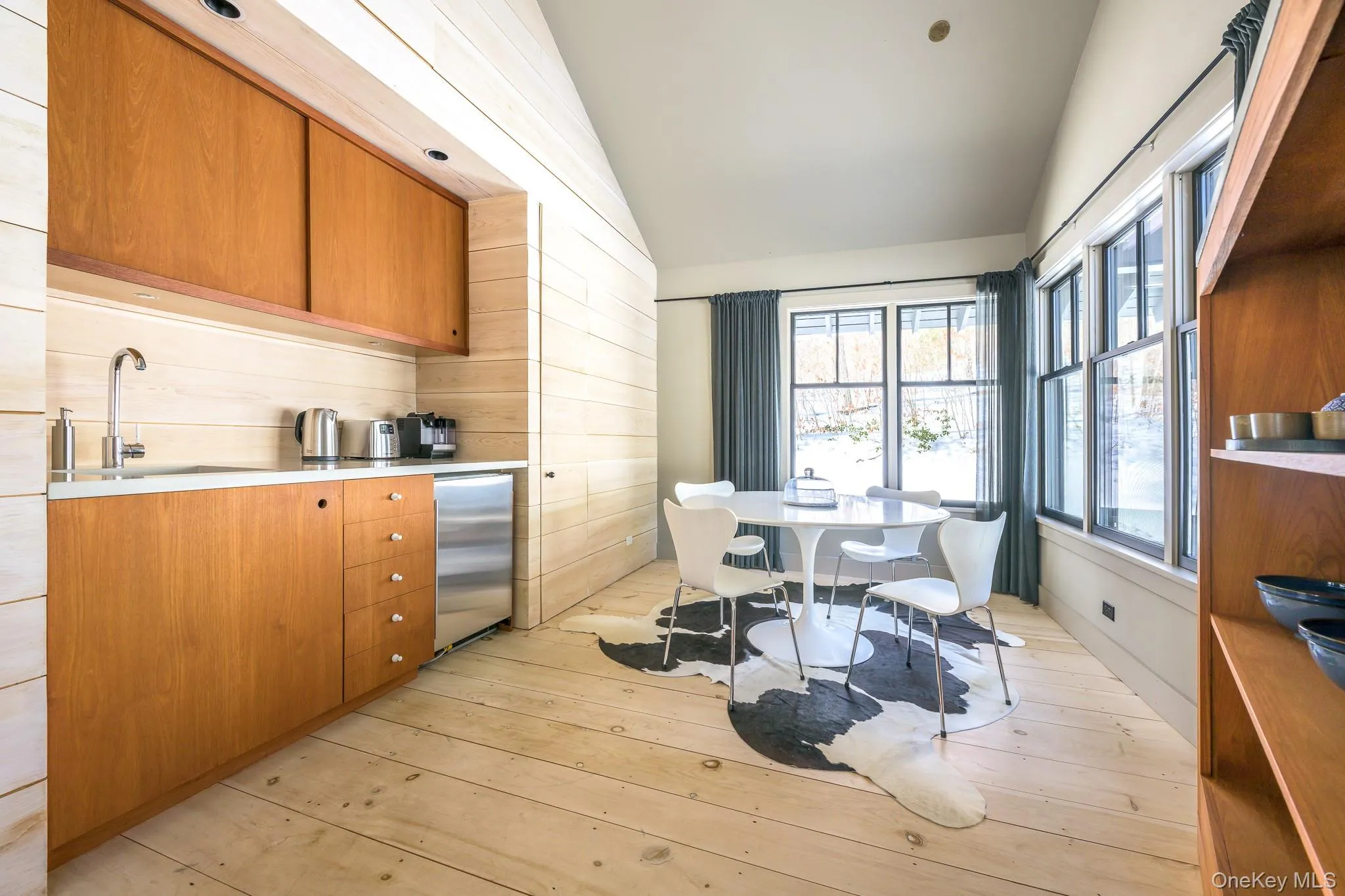 Kitchen with brown cabinets, vaulted ceiling, stainless steel fridge, light wood-type flooring, and modern cabinets Kitchen with brown cabinets, vaulted ceiling, stainless steel fridge, light wood-type flooring, and modern cabinets