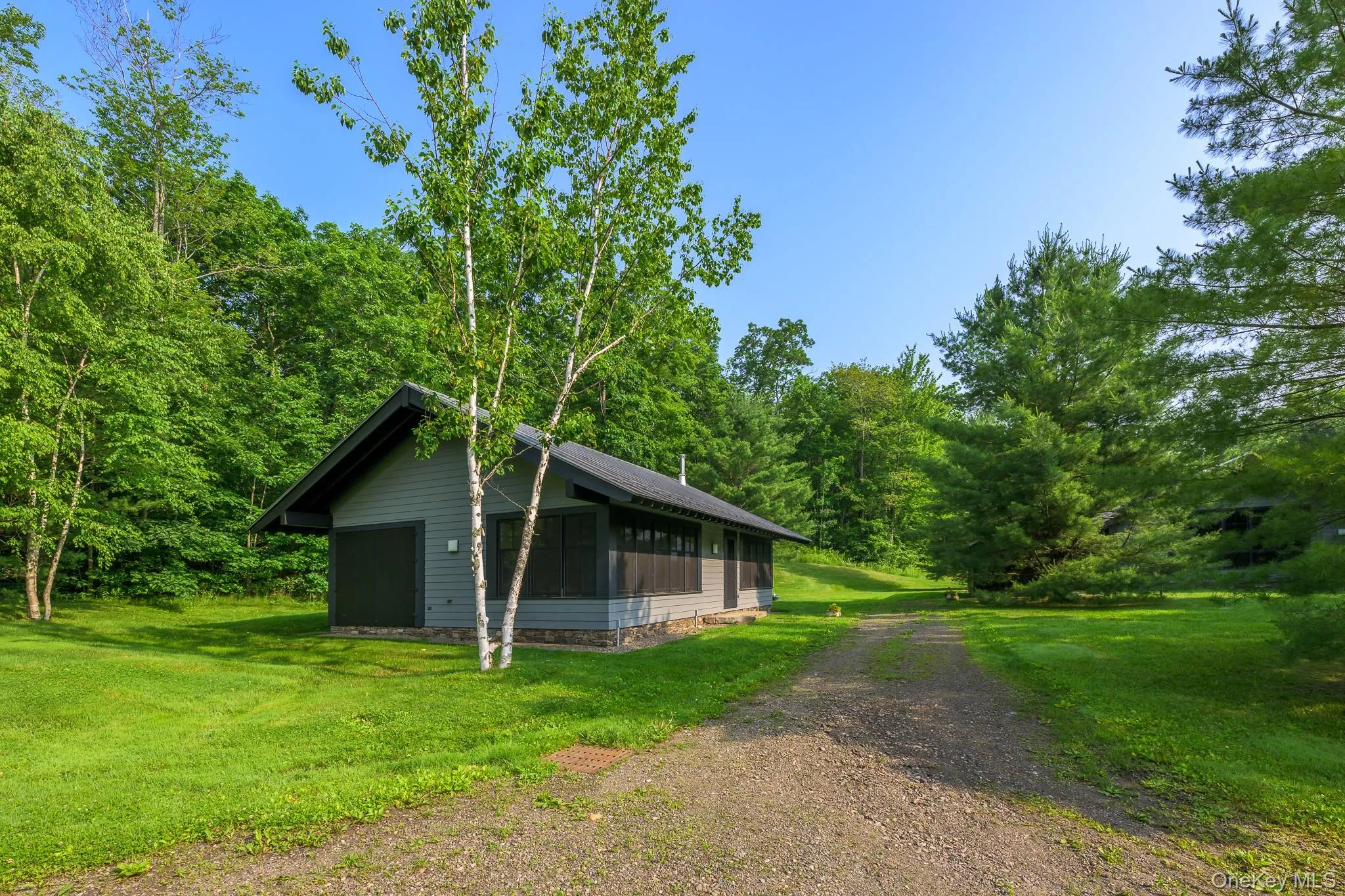 View of side of home featuring a sunroom, a lawn, dirt driveway, and a wooded view View of side of home featuring a sunroom, a lawn, dirt driveway, and a wooded view