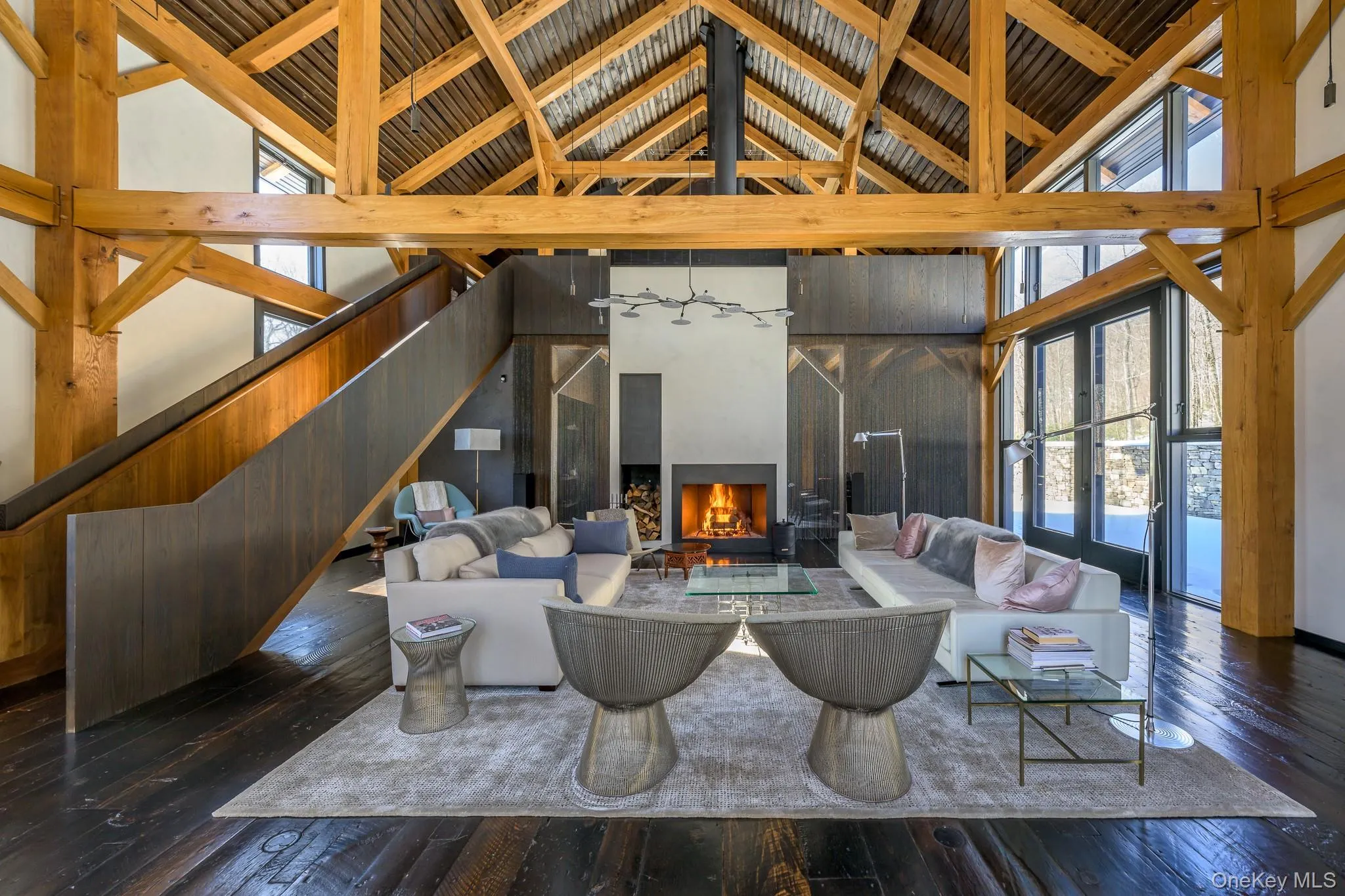 Living room with hardwood / wood-style floors, a warm lit fireplace, high vaulted ceiling, and healthy amount of natural light Living room with hardwood / wood-style floors, a warm lit fireplace, high vaulted ceiling, and healthy amount of natural light