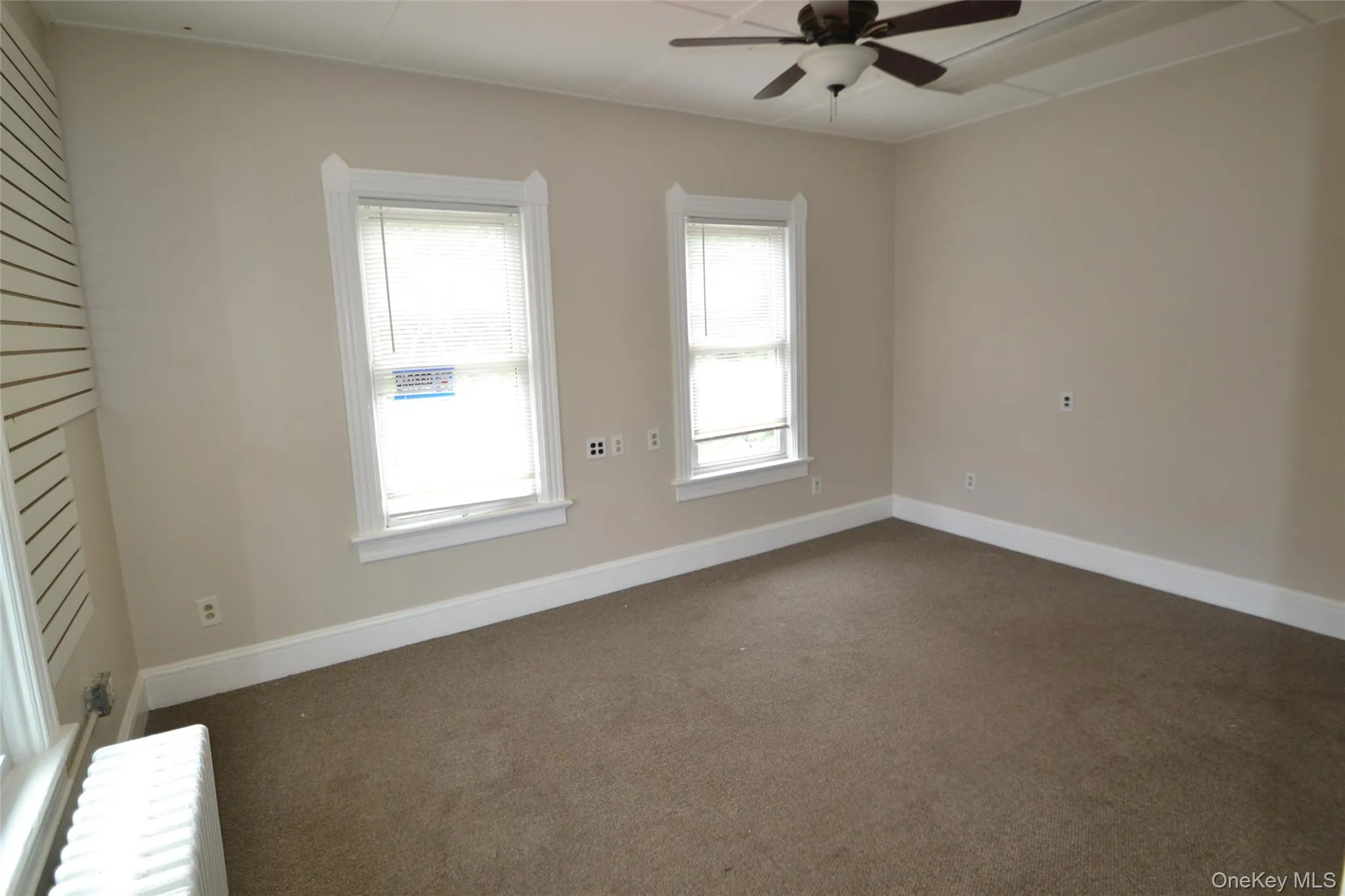 Spare room with radiator heating unit, dark carpet, and a ceiling fan Spare room with radiator heating unit, dark carpet, and a ceiling fan