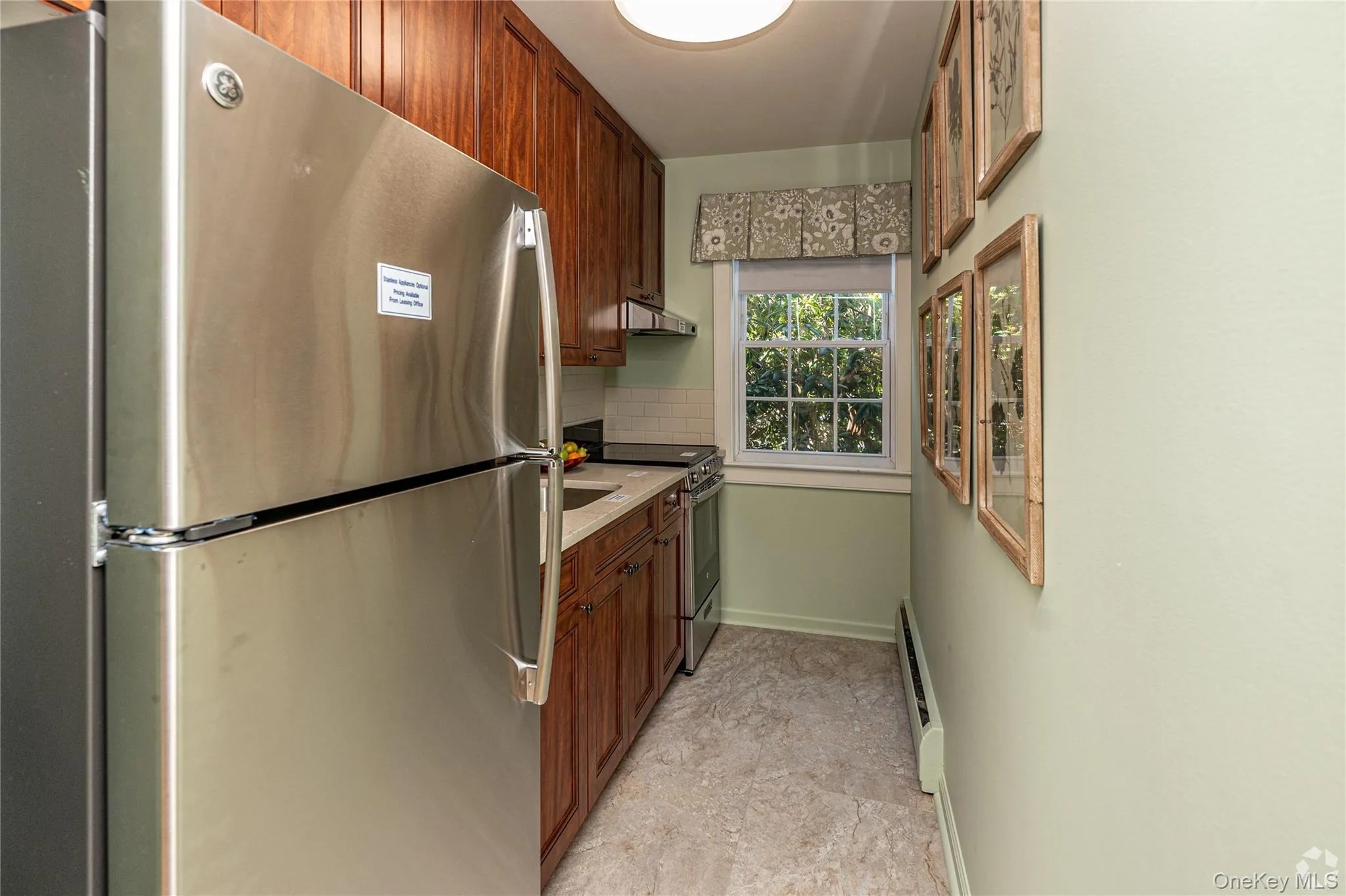 Kitchen with stainless steel appliances, brown cabinetry, tasteful backsplash, baseboard heating, and under cabinet range hood Kitchen with stainless steel appliances, brown cabinetry, tasteful backsplash, baseboard heating, and under cabinet range hood