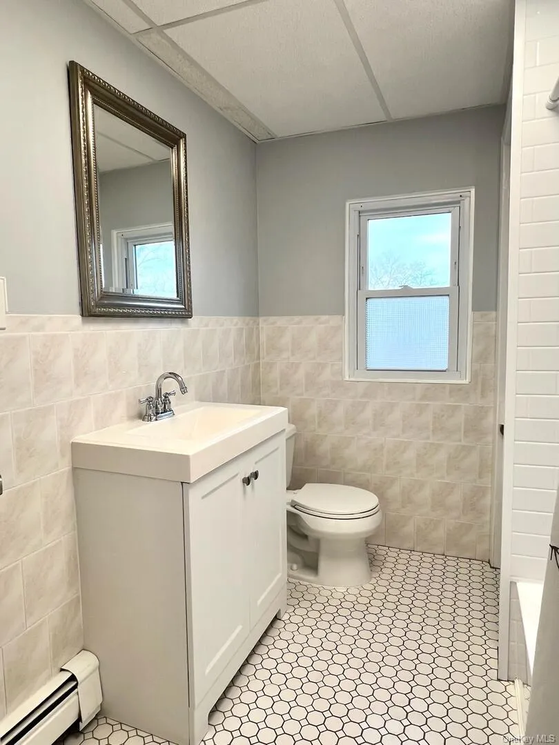 Bathroom with baseboard heating, vanity, plenty of natural light, wainscoting, and tile walls Bathroom with baseboard heating, vanity, plenty of natural light, wainscoting, and tile walls