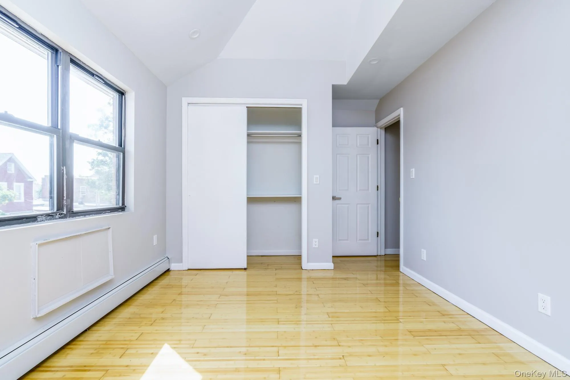 Unfurnished bedroom featuring a baseboard heating unit, light wood finished floors, vaulted ceiling, and a closet Unfurnished bedroom featuring a baseboard heating unit, light wood finished floors, vaulted ceiling, and a closet