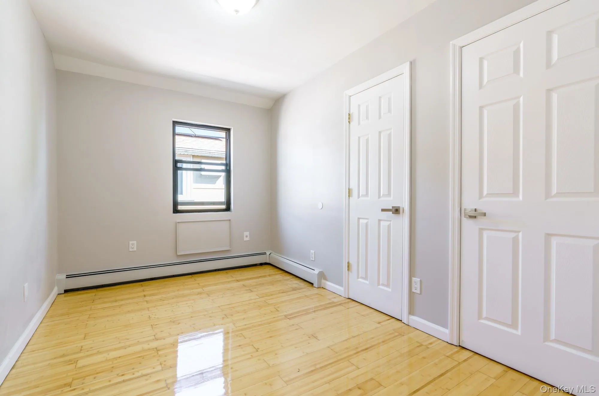 Unfurnished bedroom with baseboard heating and light wood finished floors Unfurnished bedroom with baseboard heating and light wood finished floors