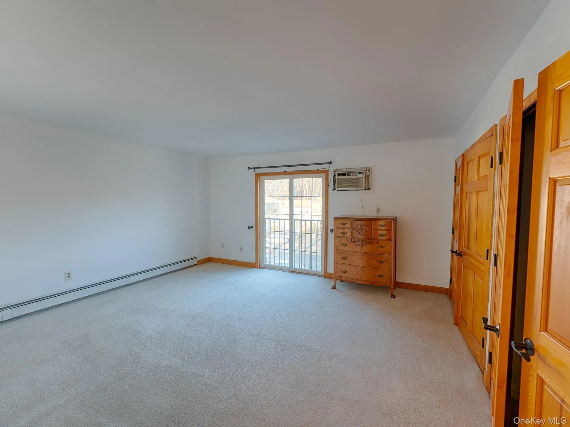 Unfurnished bedroom with light colored carpet, access to outside, a baseboard radiator, and a wall unit AC Unfurnished bedroom with light colored carpet, access to outside, a baseboard radiator, and a wall unit AC