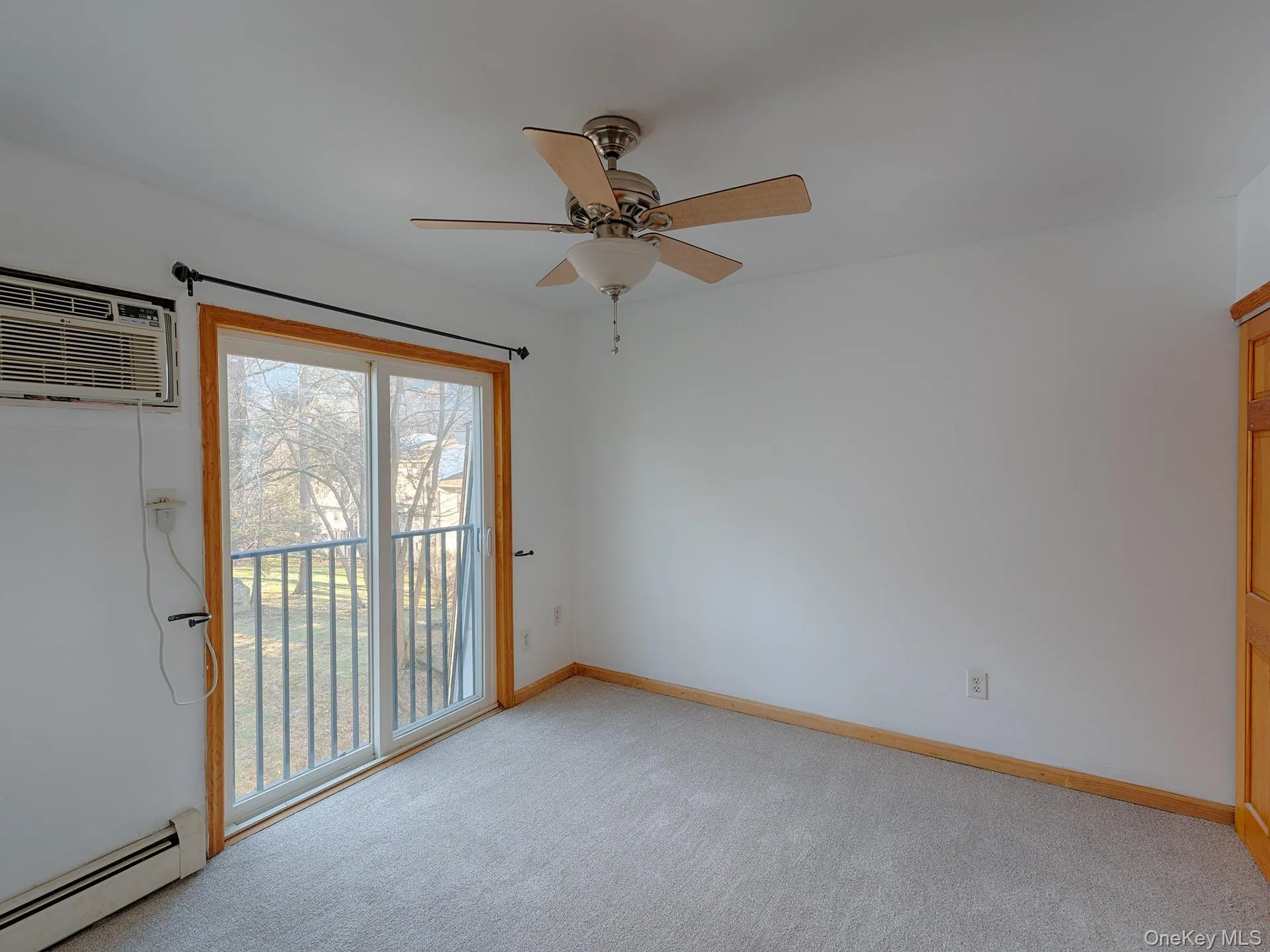 Unfurnished room with baseboard heating, light carpet, a wall unit AC, and ceiling fan Unfurnished room with baseboard heating, light carpet, a wall unit AC, and ceiling fan