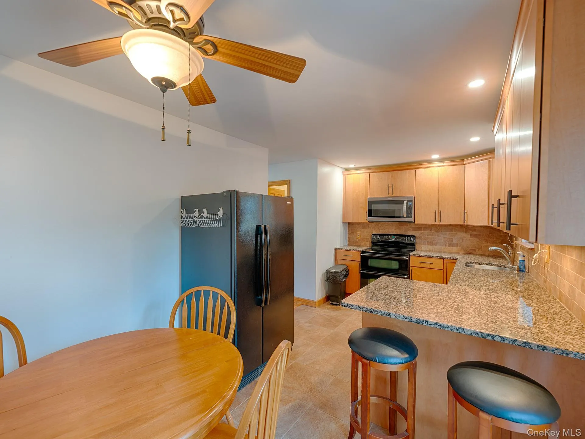Kitchen featuring light stone countertops, a peninsula, decorative backsplash, black appliances, and a kitchen breakfast bar Kitchen featuring light stone countertops, a peninsula, decorative backsplash, black appliances, and a kitchen breakfast bar