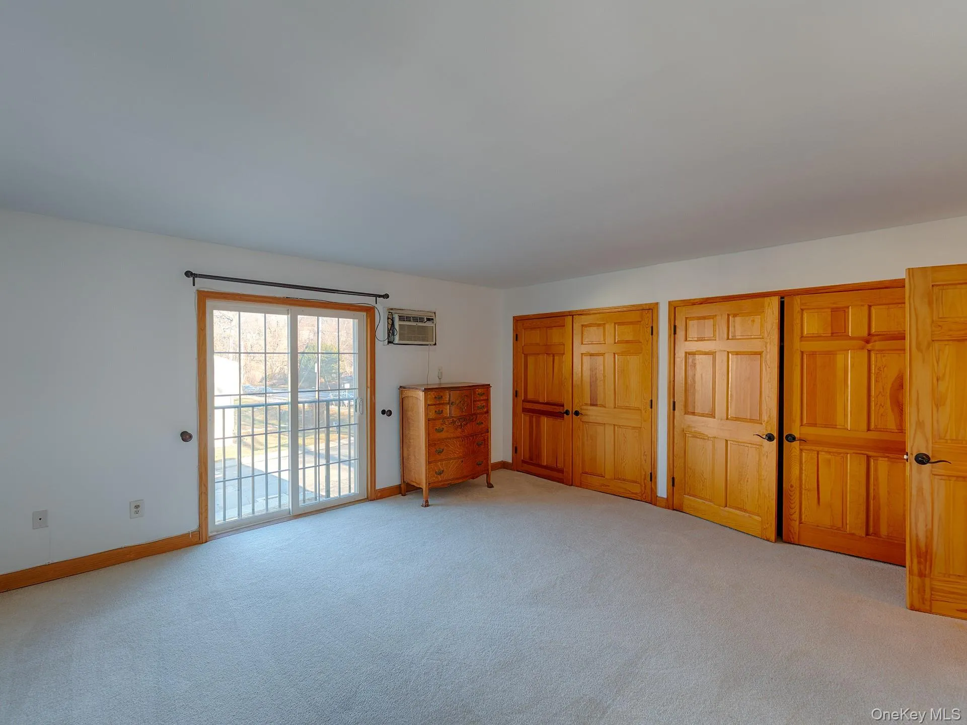 Unfurnished bedroom with multiple closets, light carpet, access to outside, and a wall mounted AC Unfurnished bedroom with multiple closets, light carpet, access to outside, and a wall mounted AC