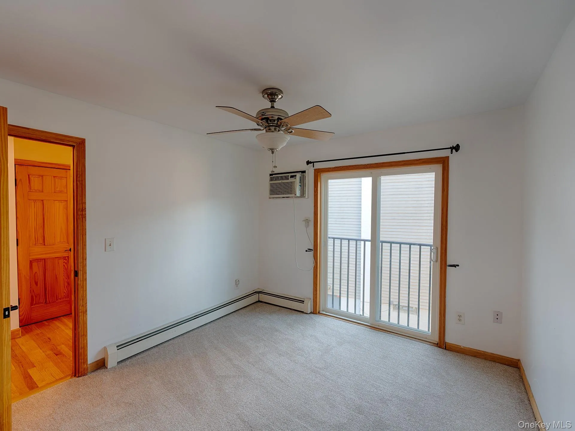 Unfurnished room with light carpet, a ceiling fan, a baseboard radiator, and a wall mounted AC Unfurnished room with light carpet, a ceiling fan, a baseboard radiator, and a wall mounted AC