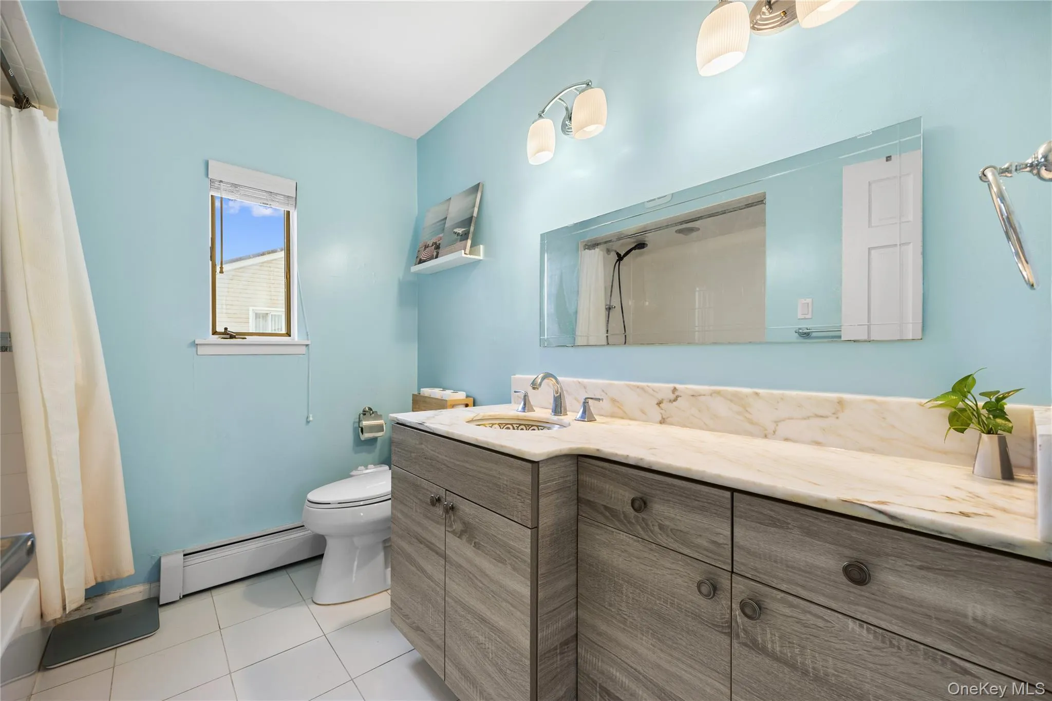 Full bath featuring vanity, a baseboard heating unit, light tile patterned floors, and shower / bath combination with curtain Full bath featuring vanity, a baseboard heating unit, light tile patterned floors, and shower / bath combination with curtain
