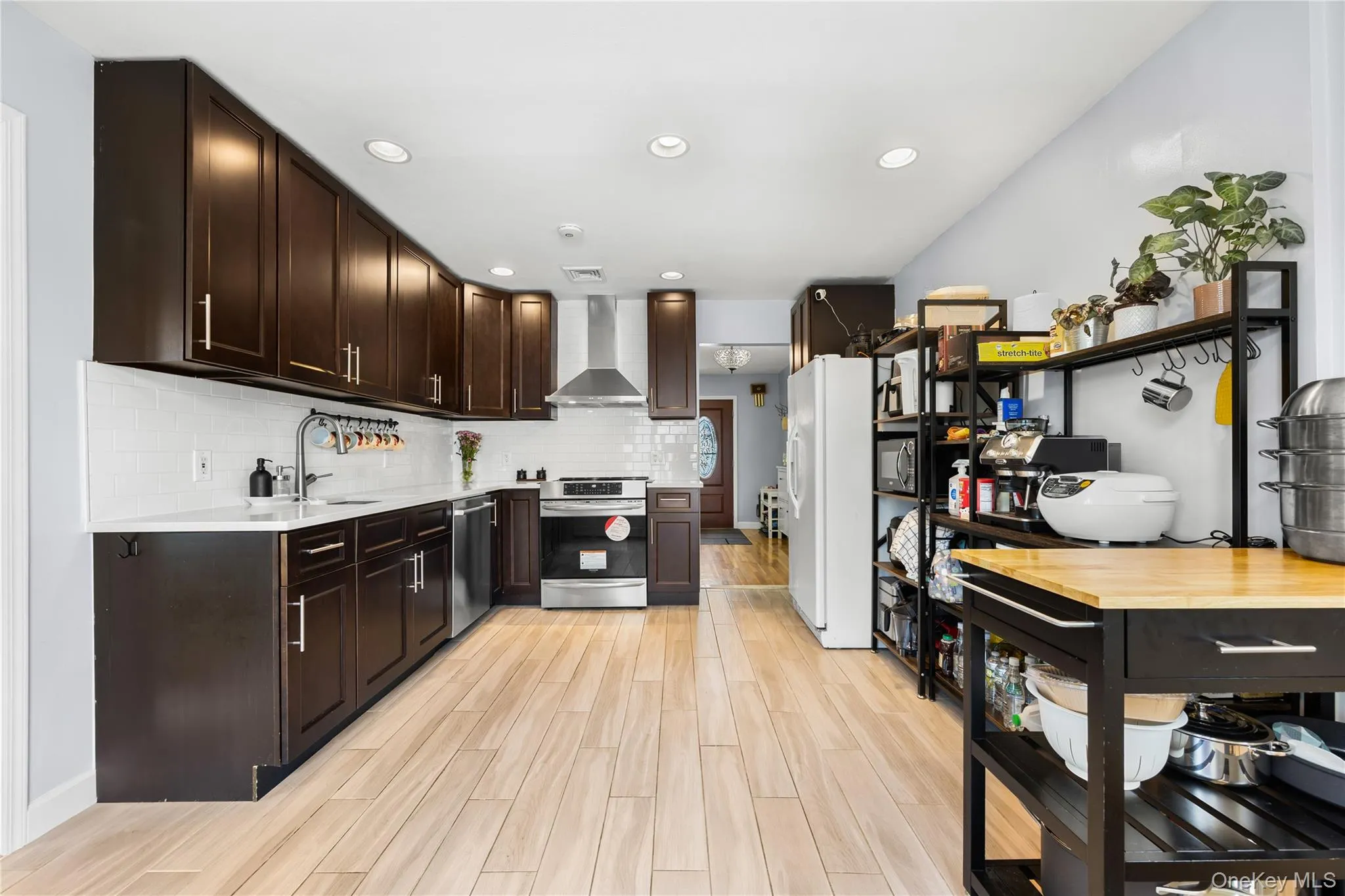 Kitchen with dark brown cabinets, stainless steel appliances, wall chimney exhaust hood, decorative backsplash, and recessed lighting Kitchen with dark brown cabinets, stainless steel appliances, wall chimney exhaust hood, decorative backsplash, and recessed lighting