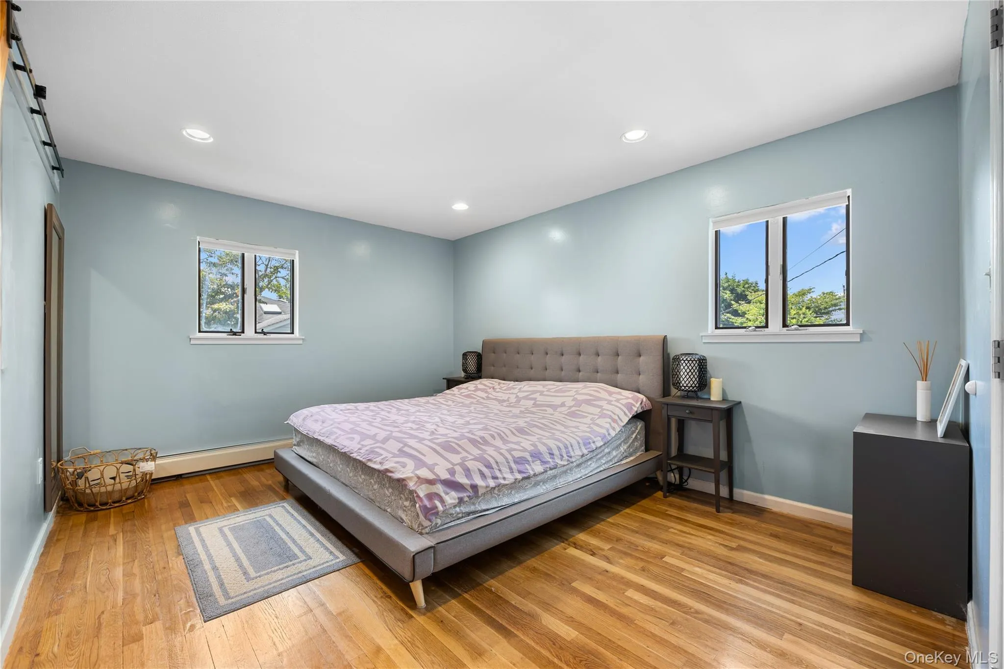 Bedroom with a barn door, light wood-style flooring, multiple windows, and recessed lighting Bedroom with a barn door, light wood-style flooring, multiple windows, and recessed lighting