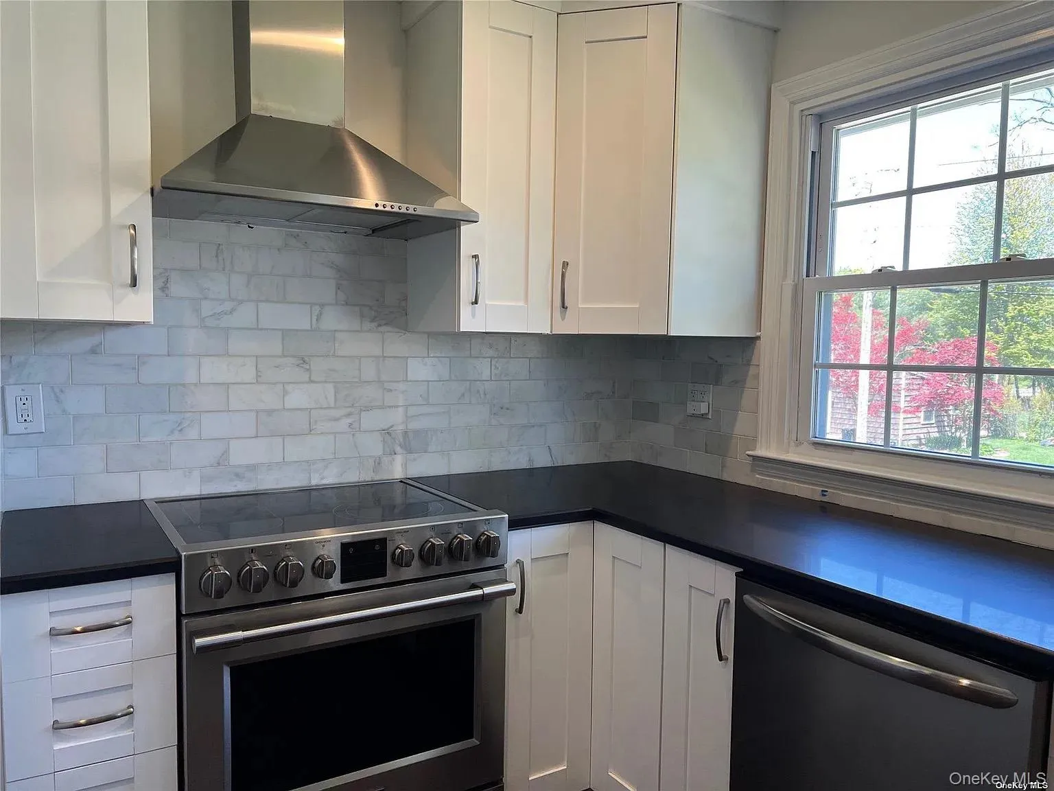 Kitchen featuring appliances with stainless steel finishes, wall chimney exhaust hood, white cabinets, and decorative backsplash Kitchen featuring appliances with stainless steel finishes, wall chimney exhaust hood, white cabinets, and decorative backsplash