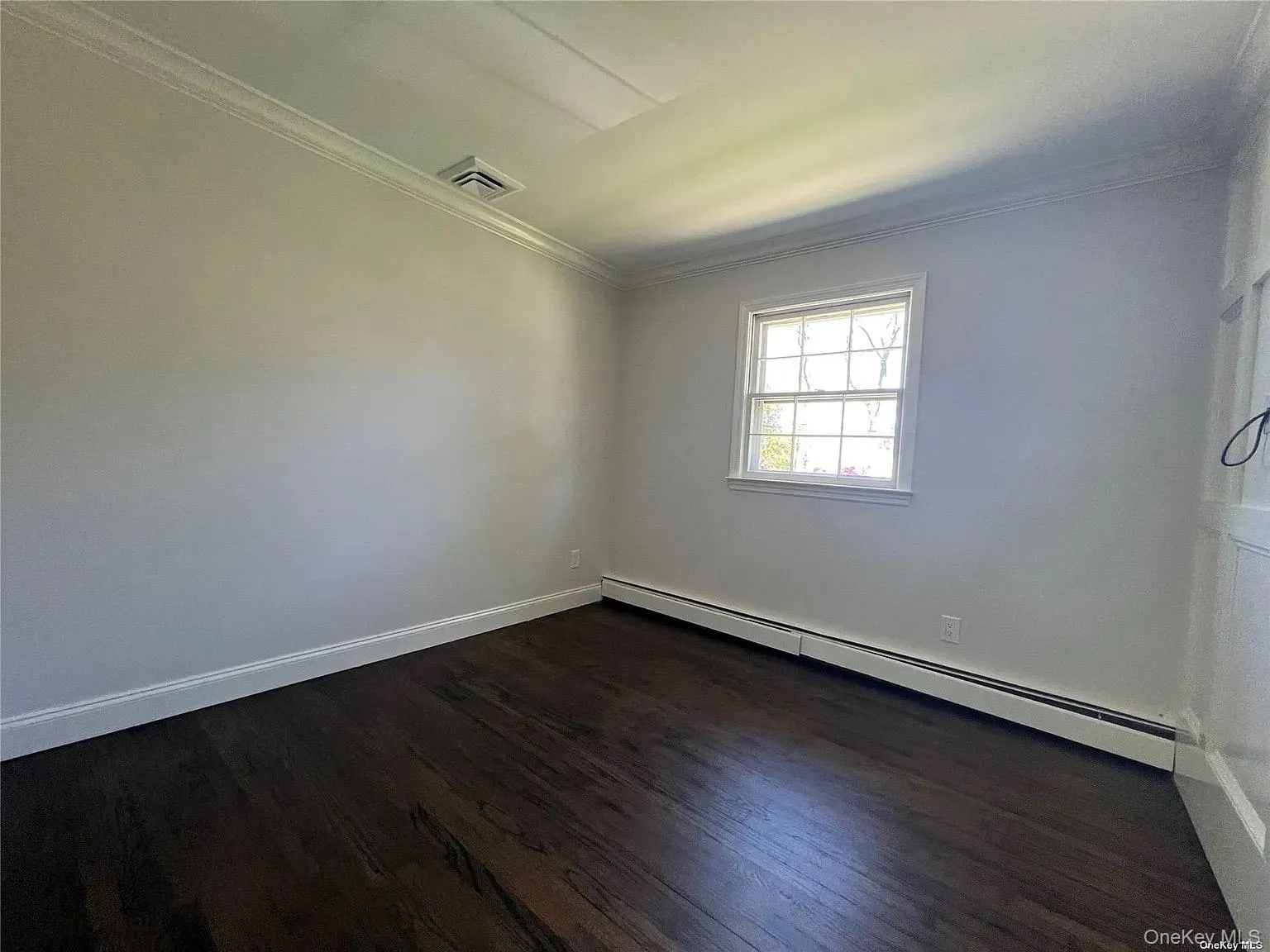 Empty room featuring baseboard heating, dark wood-style flooring, and ornamental molding Empty room featuring baseboard heating, dark wood-style flooring, and ornamental molding