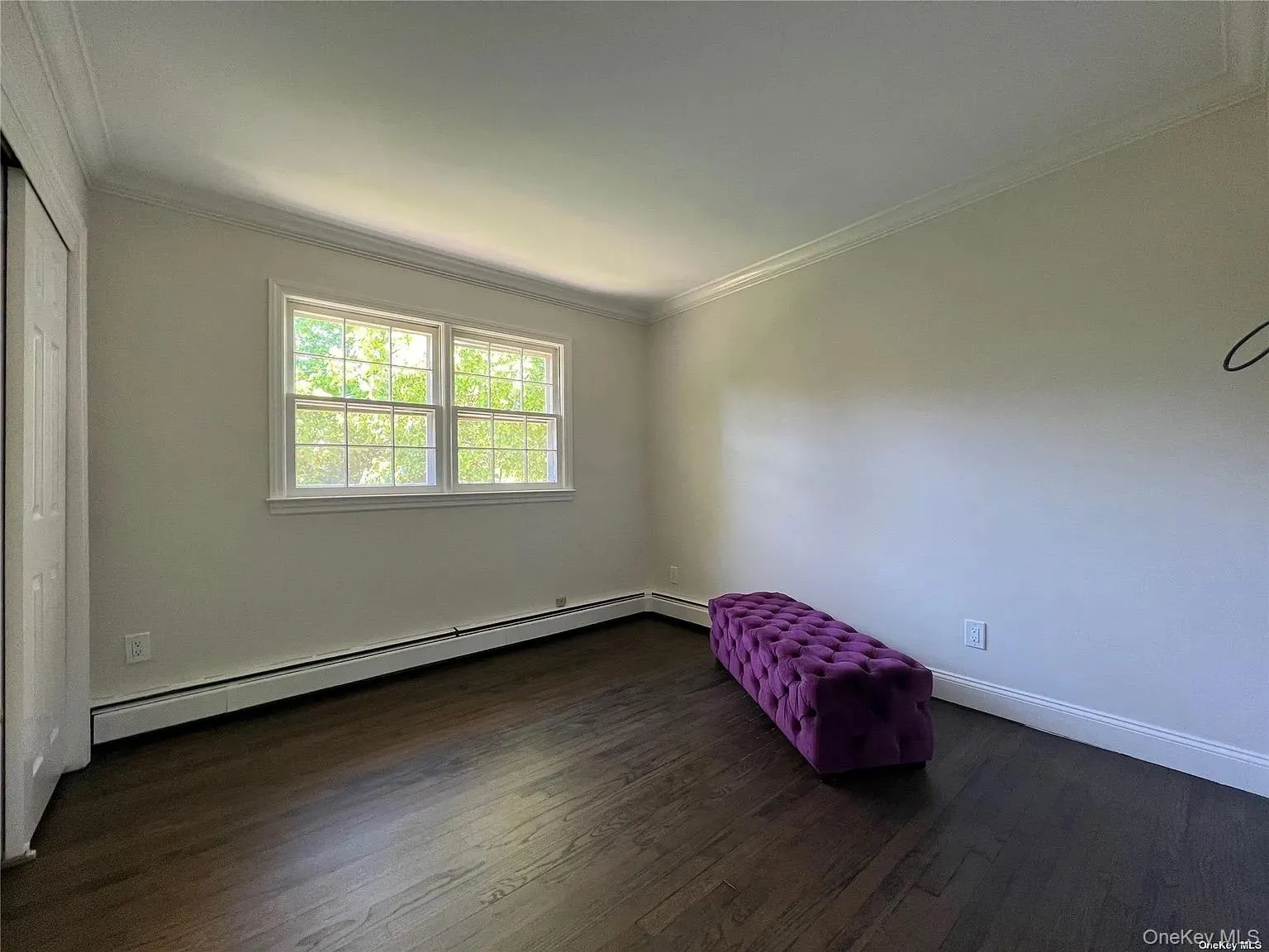 Unfurnished bedroom with baseboard heating, ornamental molding, and dark wood-style floors Unfurnished bedroom with baseboard heating, ornamental molding, and dark wood-style floors
