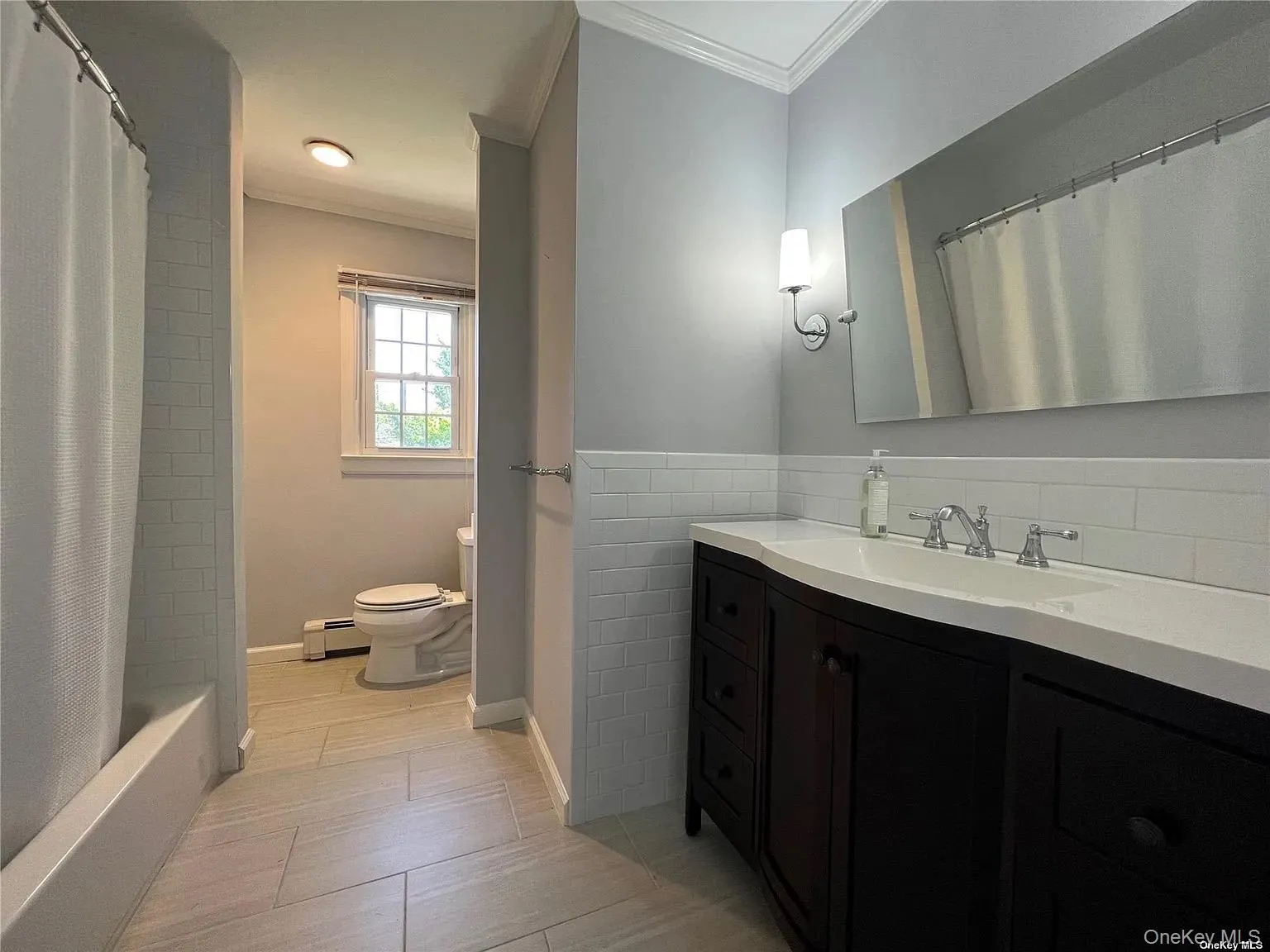 Full bathroom with crown molding, vanity, a baseboard heating unit, and shower / tub combo with curtain Full bathroom with crown molding, vanity, a baseboard heating unit, and shower / tub combo with curtain
