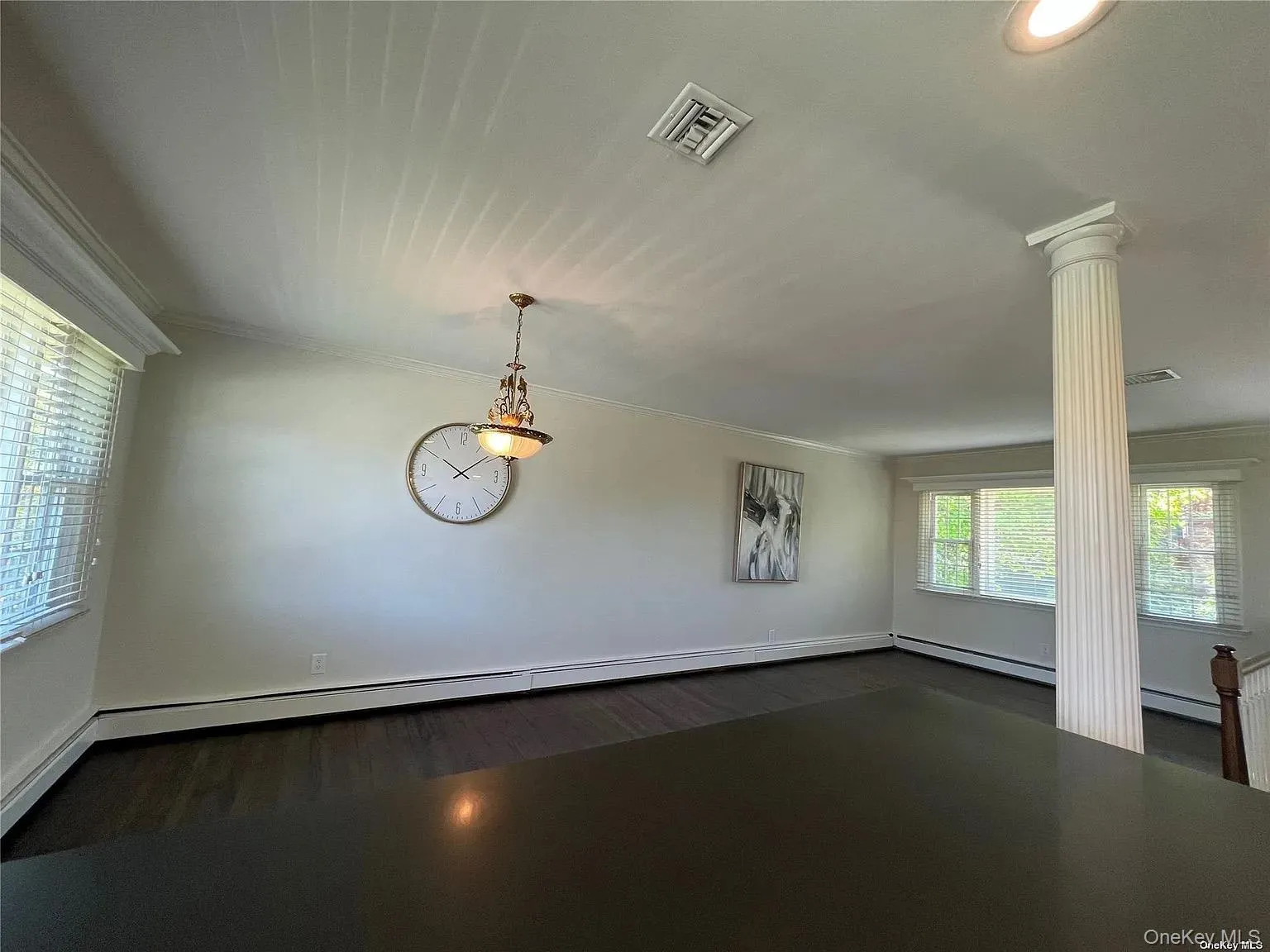 Unfurnished room with crown molding, dark wood-type flooring, decorative columns, and a baseboard radiator Unfurnished room with crown molding, dark wood-type flooring, decorative columns, and a baseboard radiator