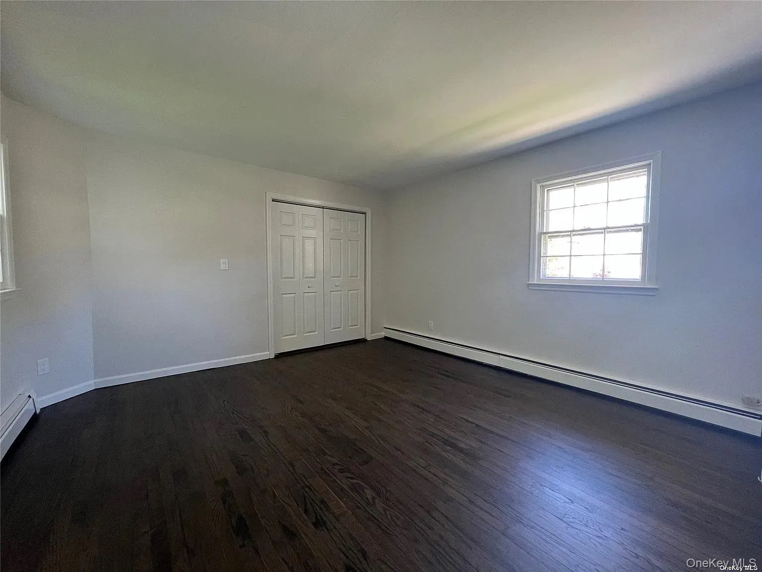 Unfurnished bedroom with baseboard heating, a closet, and dark wood-type flooring Unfurnished bedroom with baseboard heating, a closet, and dark wood-type flooring