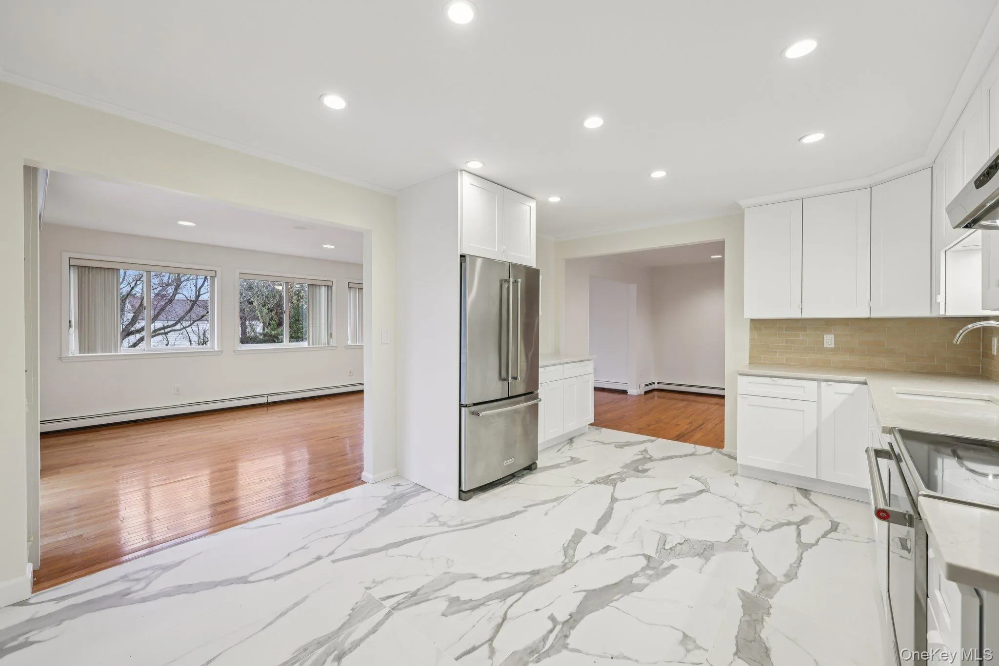 Renovated kitchen featuring light marble finish floors, stainless steel appliances, white cabinetry, light stone counters, and recessed lighting Renovated kitchen featuring light marble finish floors, stainless steel appliances, white cabinetry, light stone counters, and recessed lighting