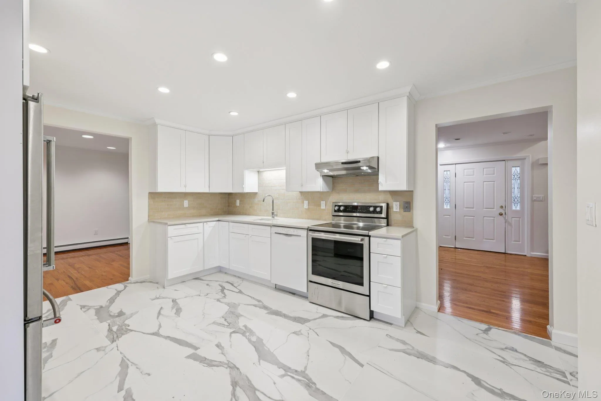 Renovated kitchen with light marble finish floors, appliances with stainless steel finishes, white cabinetry, ornamental molding, and recessed lighting Renovated kitchen with light marble finish floors, appliances with stainless steel finishes, white cabinetry, ornamental molding, and recessed lighting