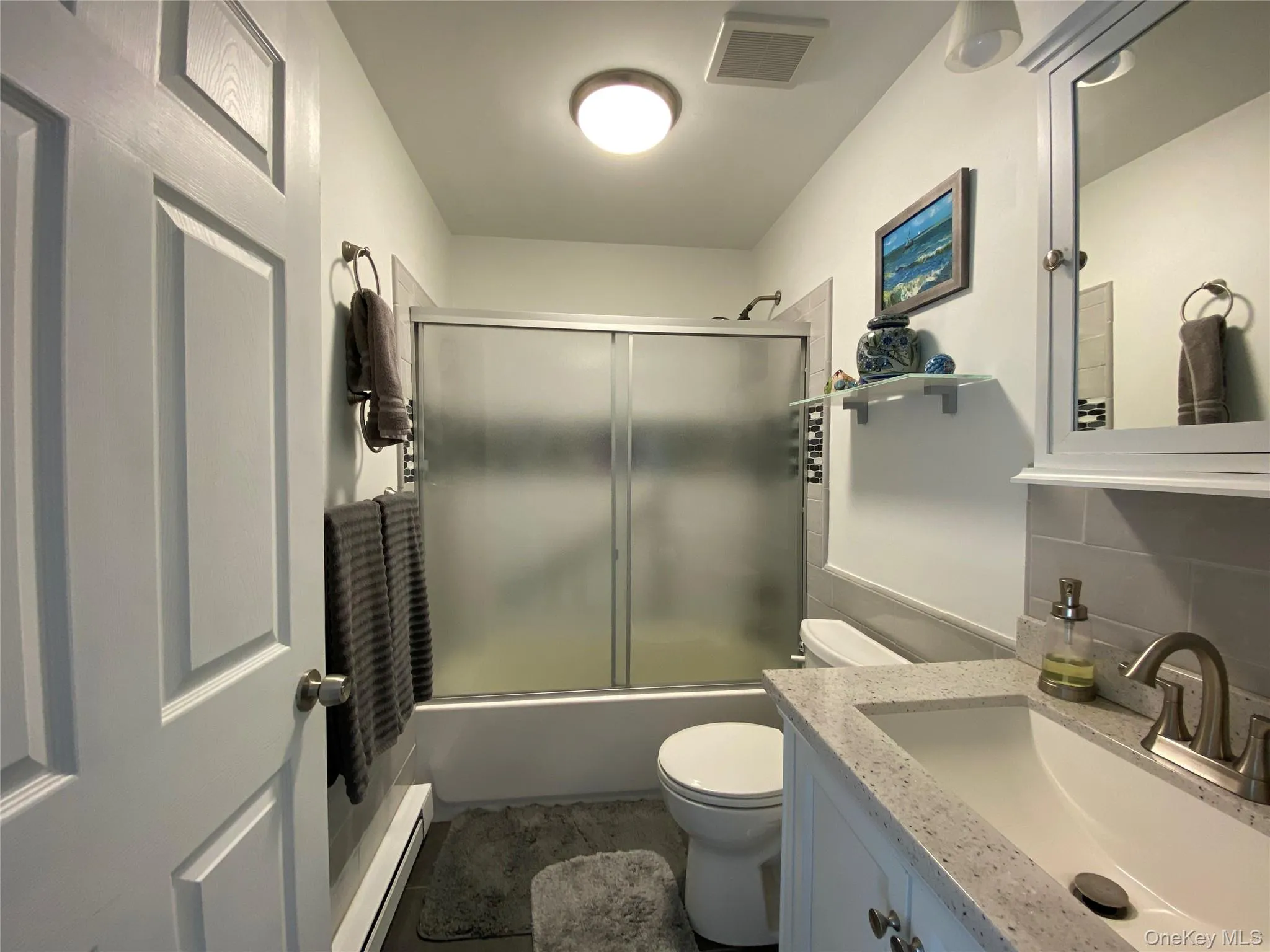 Full bathroom featuring a baseboard heating unit, bath / shower combo with glass door, and vanity Full bathroom featuring a baseboard heating unit, bath / shower combo with glass door, and vanity