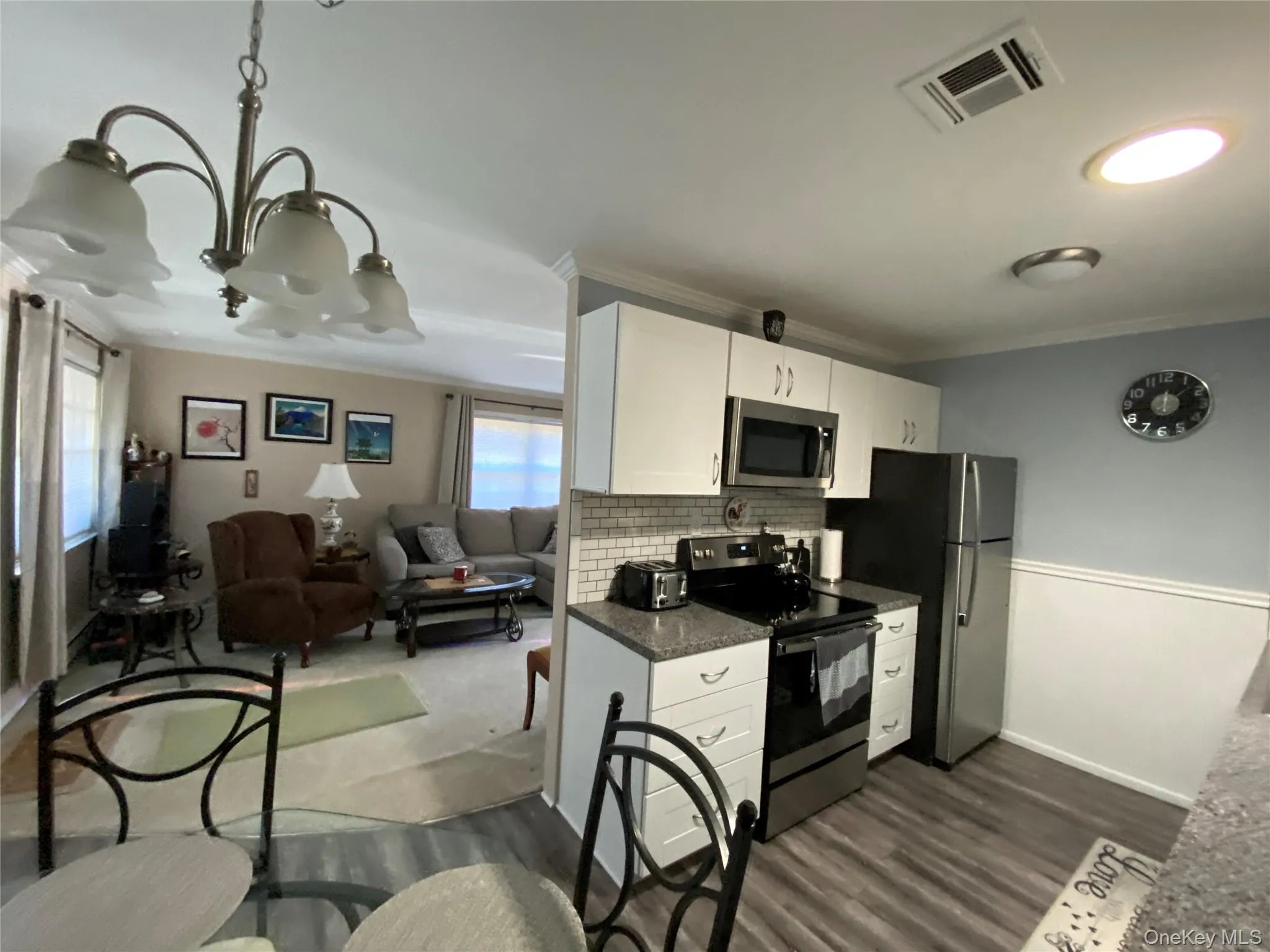 Kitchen featuring electric range oven, open floor plan, white cabinets, stainless steel microwave, and tasteful backsplash Kitchen featuring electric range oven, open floor plan, white cabinets, stainless steel microwave, and tasteful backsplash