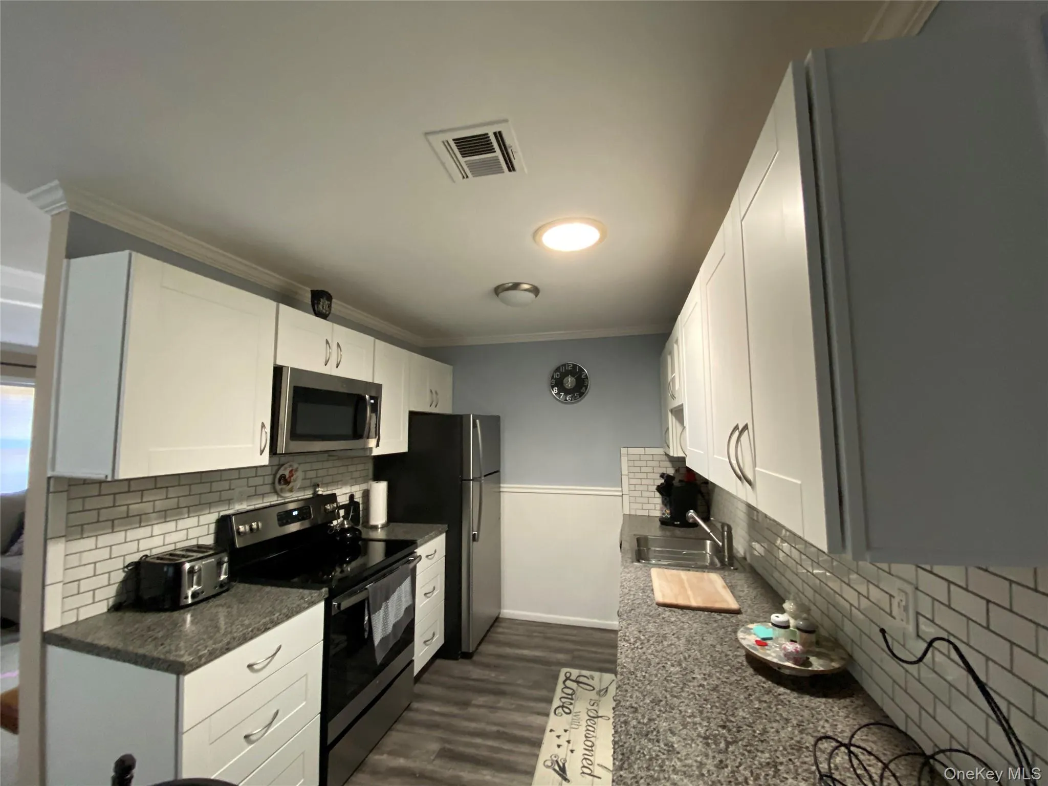 Kitchen featuring backsplash, appliances with stainless steel finishes, white cabinets, dark wood-style floors, and ornamental molding Kitchen featuring backsplash, appliances with stainless steel finishes, white cabinets, dark wood-style floors, and ornamental molding