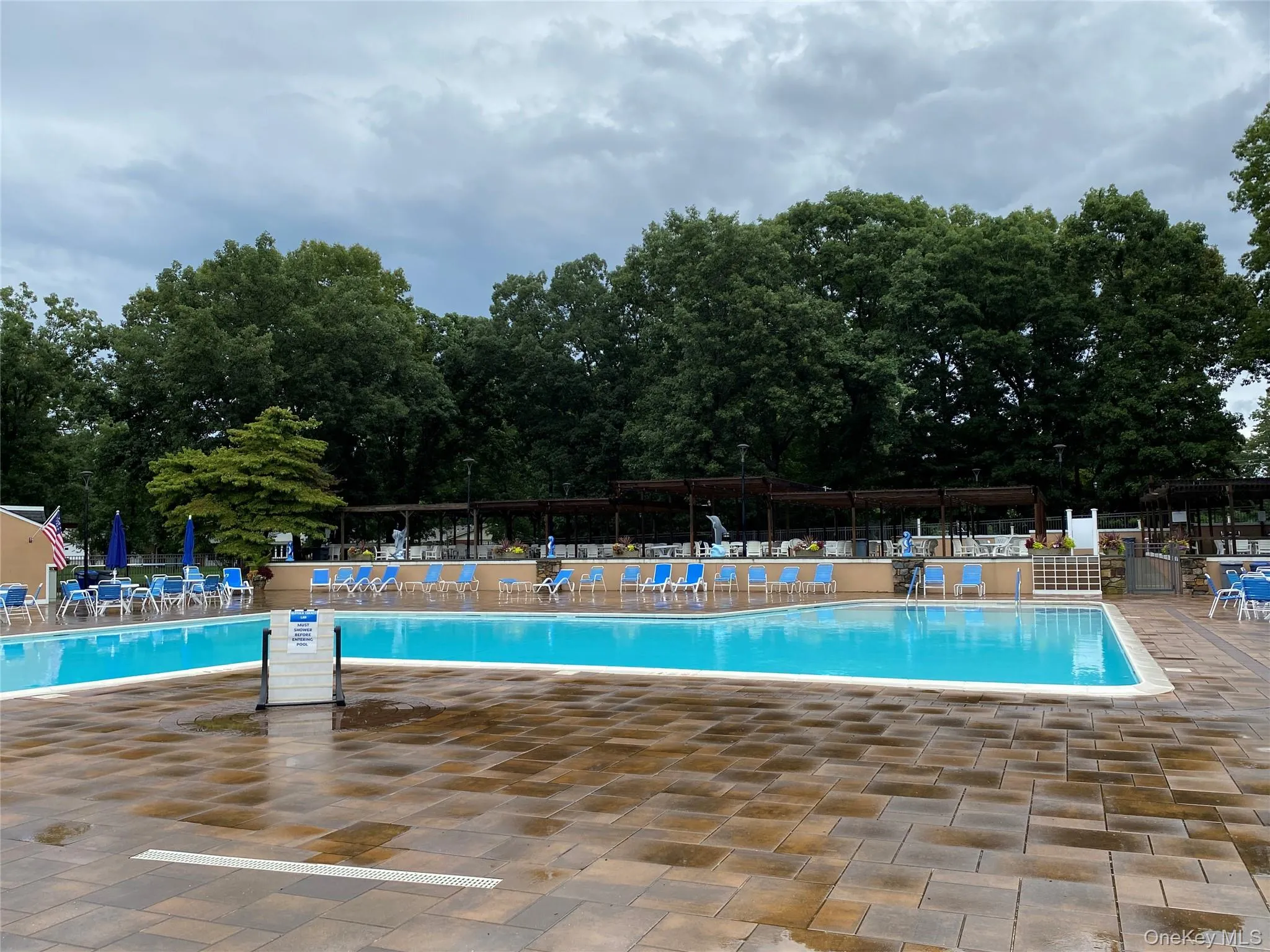 Expansive outdoor pool area featuring two distinct pool sections, a surrounding paver patio, and shaded seating areas with pergolas and umbrellas Expansive outdoor pool area featuring two distinct pool sections, a surrounding paver patio, and shaded seating areas with pergolas and umbrellas