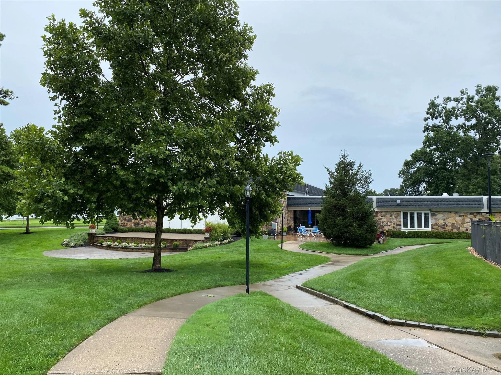 Landscaped grounds featuring a stone-clad building with white-framed windows, a paved patio, and mature trees Landscaped grounds featuring a stone-clad building with white-framed windows, a paved patio, and mature trees