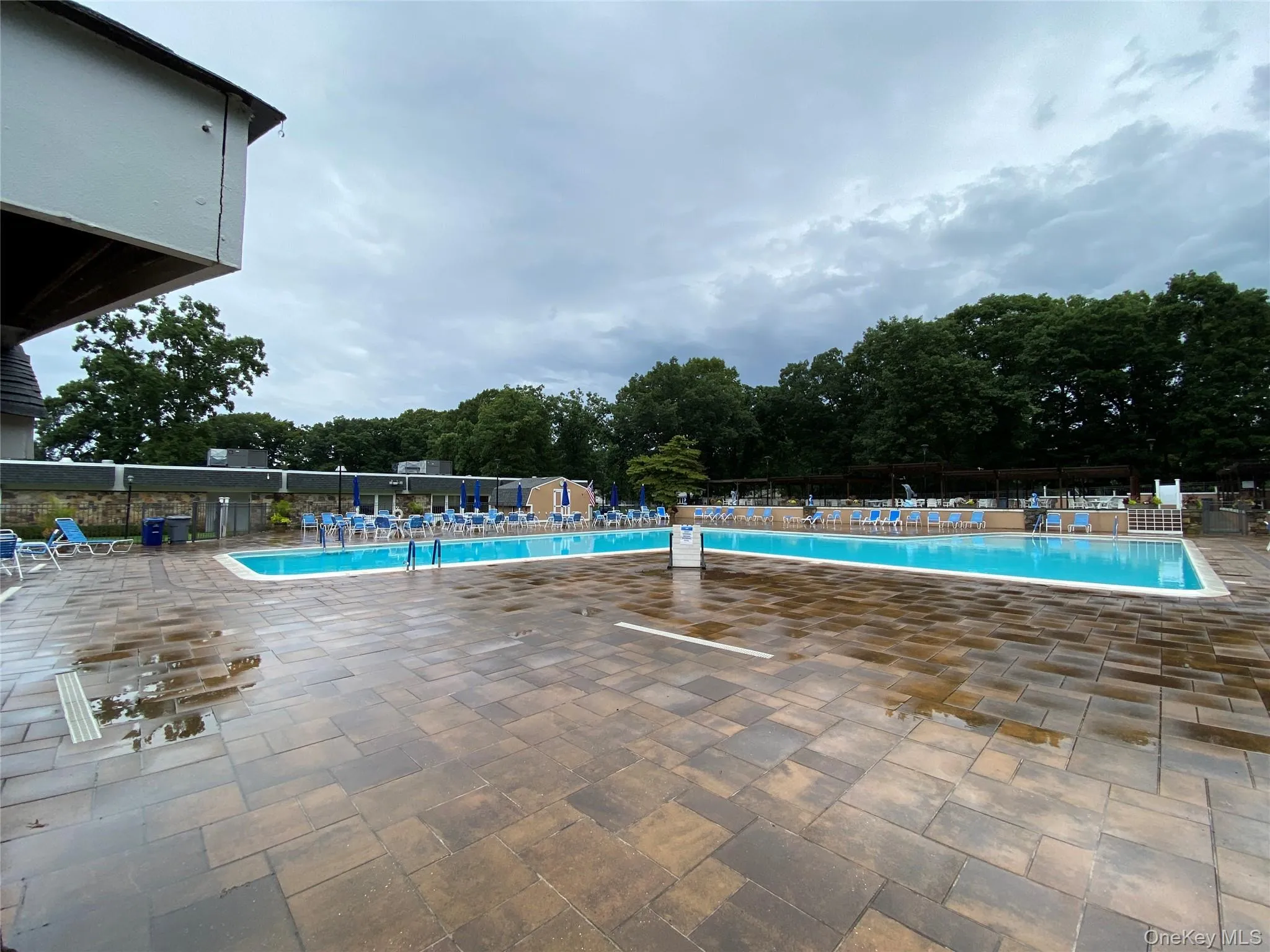 Expansive outdoor pool area featuring a paver patio and two distinct swimming pools Expansive outdoor pool area featuring a paver patio and two distinct swimming pools