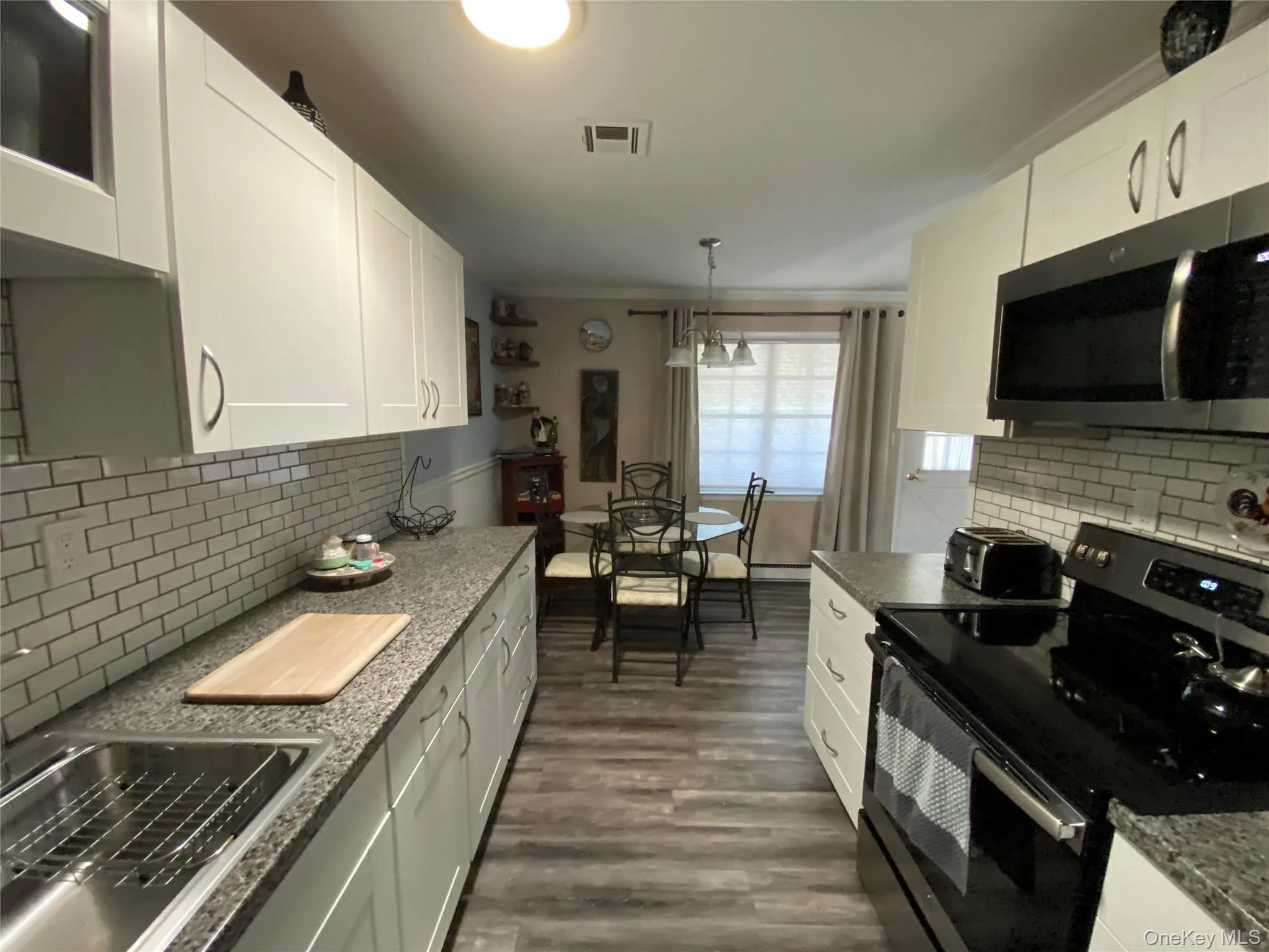 Kitchen featuring black range with electric stovetop, decorative backsplash, stainless steel microwave, white cabinetry, and crown molding Kitchen featuring black range with electric stovetop, decorative backsplash, stainless steel microwave, white cabinetry, and crown molding