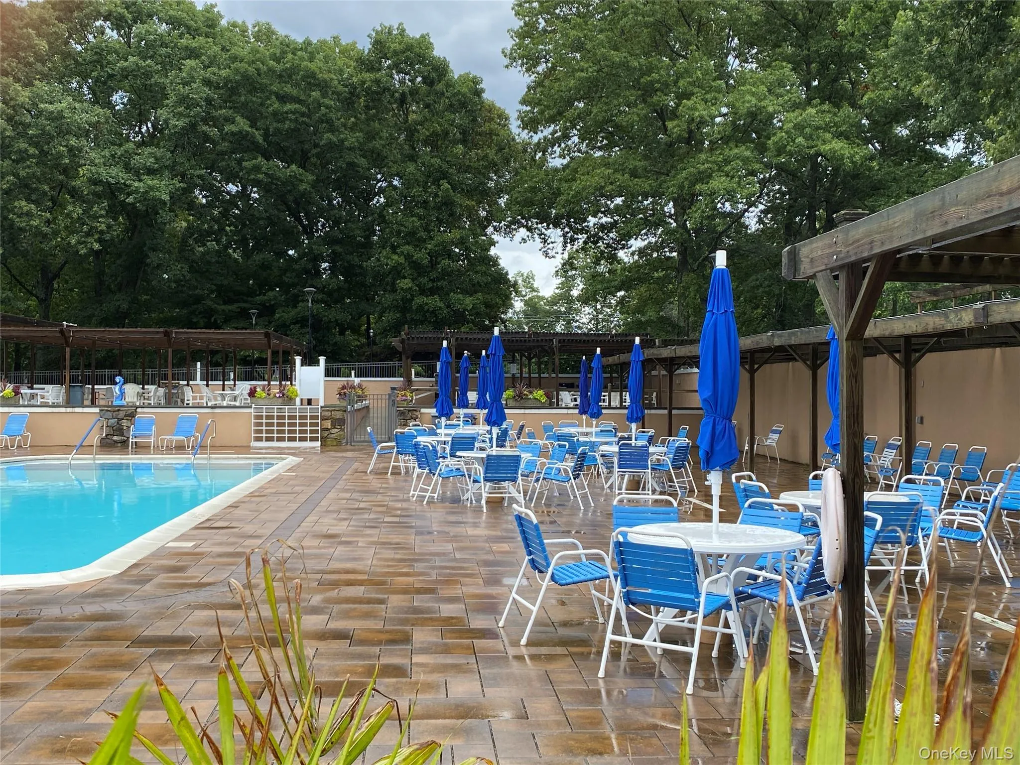 Expansive pool deck featuring a swimming pool, patterned paver surfacing, and multiple pergola structures Expansive pool deck featuring a swimming pool, patterned paver surfacing, and multiple pergola structures