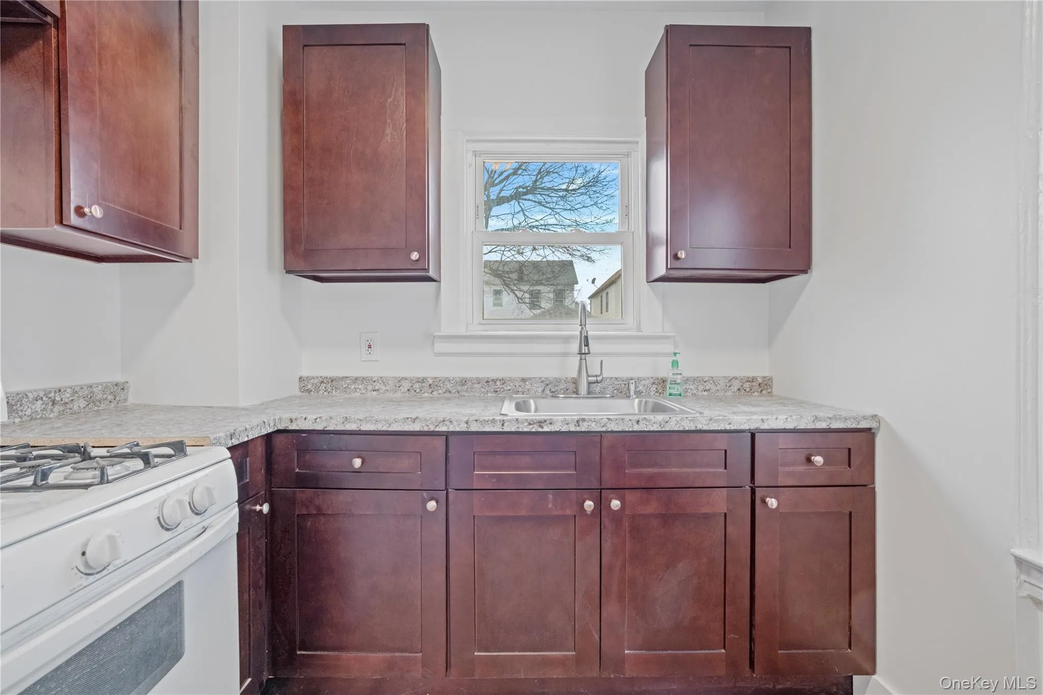 Kitchen featuring white gas range oven, dark brown cabinets, and light stone countertops Kitchen featuring white gas range oven, dark brown cabinets, and light stone countertops