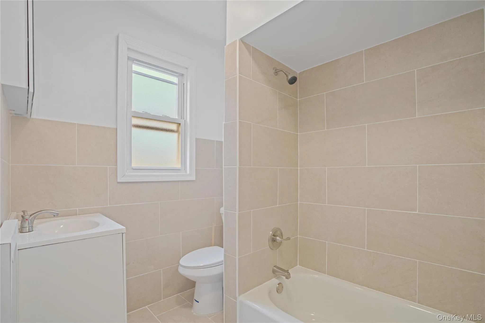 Bathroom with vanity, tile walls, shower / bath combination, a wainscoted wall, and tile patterned floors Bathroom with vanity, tile walls, shower / bath combination, a wainscoted wall, and tile patterned floors