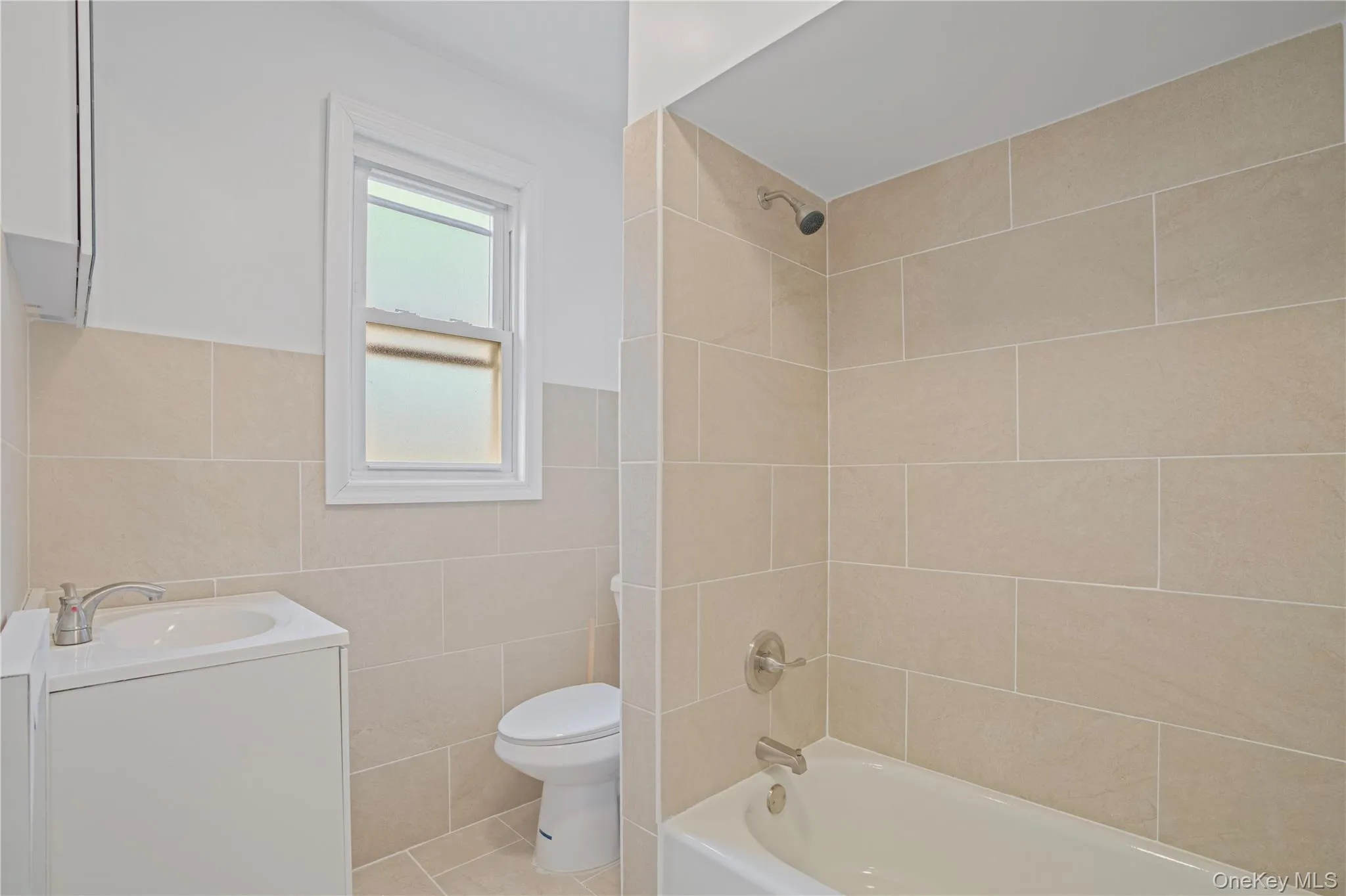 Full bath with vanity, tile walls, shower / bath combination, tile patterned flooring, and wainscoting Full bath with vanity, tile walls, shower / bath combination, tile patterned flooring, and wainscoting