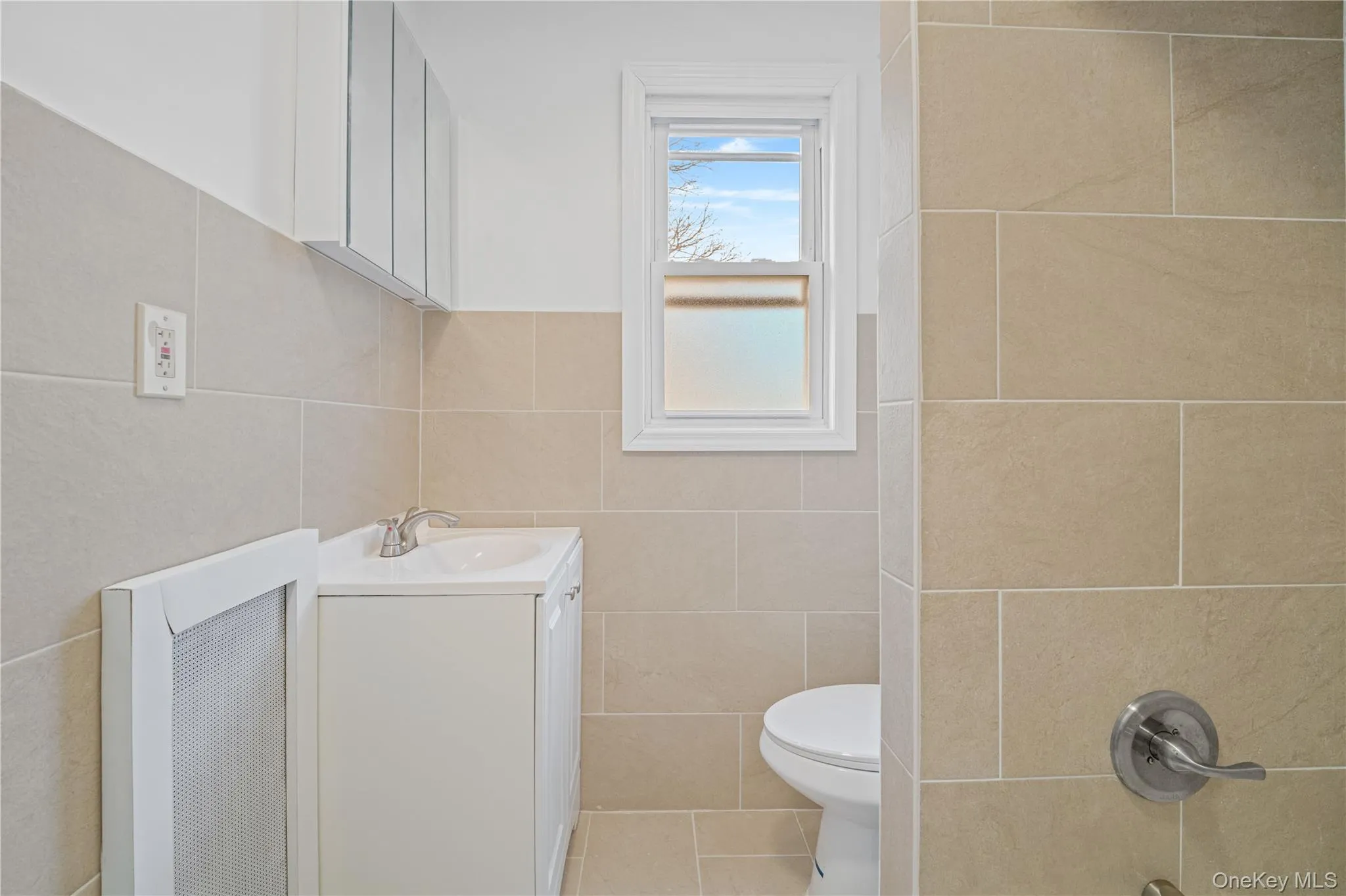 Full bathroom with vanity, tile walls, heating unit, washtub / shower combination, and tile patterned flooring Full bathroom with vanity, tile walls, heating unit, washtub / shower combination, and tile patterned flooring