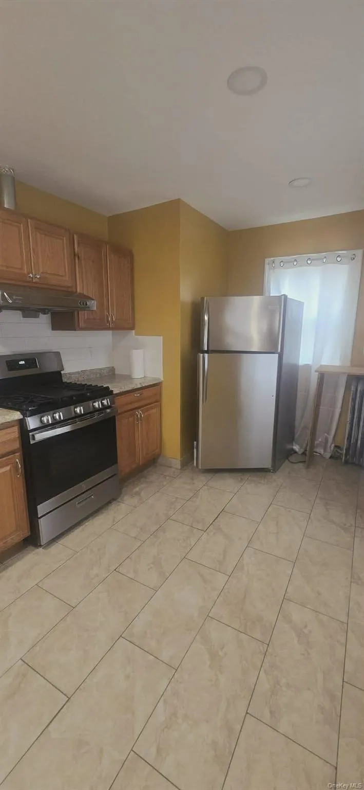 Kitchen featuring stainless steel appliances, brown cabinetry, under cabinet range hood, and decorative backsplash Kitchen featuring stainless steel appliances, brown cabinetry, under cabinet range hood, and decorative backsplash