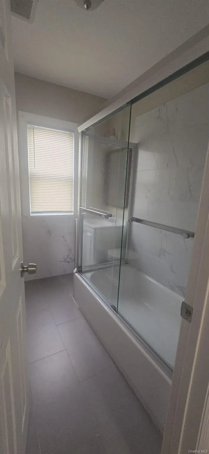 Full bath with shower / bath combination with glass door and tile patterned floors Full bath with shower / bath combination with glass door and tile patterned floors