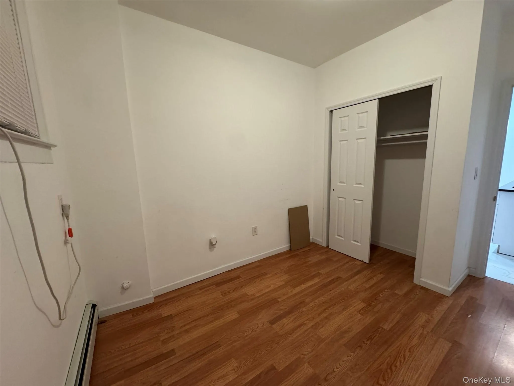 Unfurnished bedroom featuring a baseboard heating unit, wood finished floors, and a closet Unfurnished bedroom featuring a baseboard heating unit, wood finished floors, and a closet
