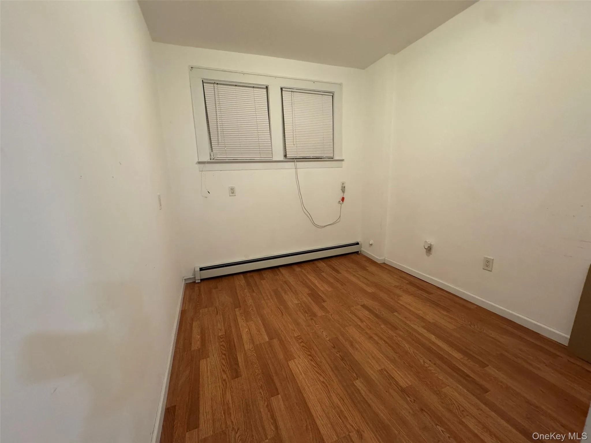 Empty room with baseboard heating and wood finished floors Empty room with baseboard heating and wood finished floors