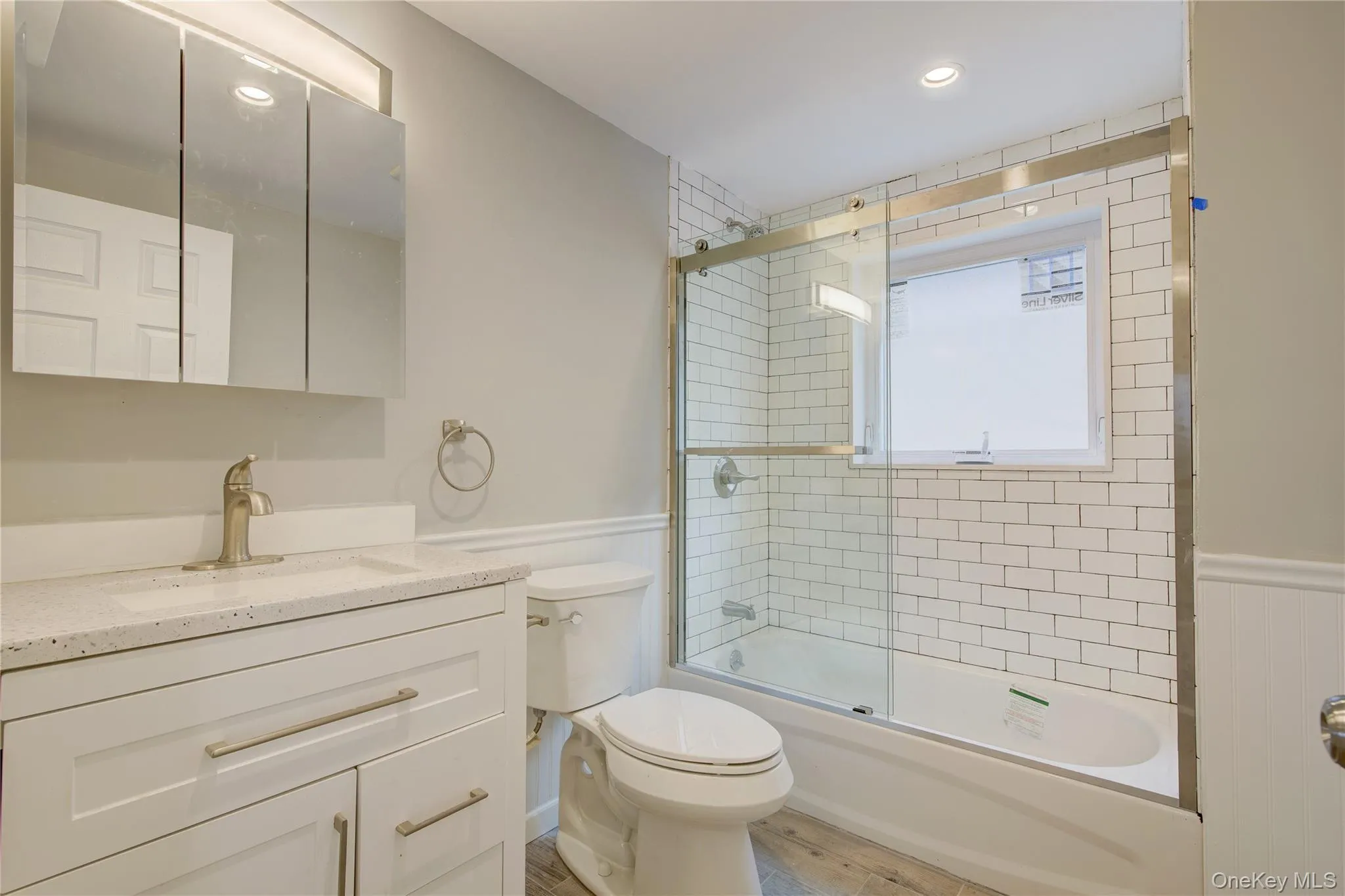 Full bath with wainscoting, vanity, enclosed tub / shower combo, wood finished floors, and recessed lighting Full bath with wainscoting, vanity, enclosed tub / shower combo, wood finished floors, and recessed lighting