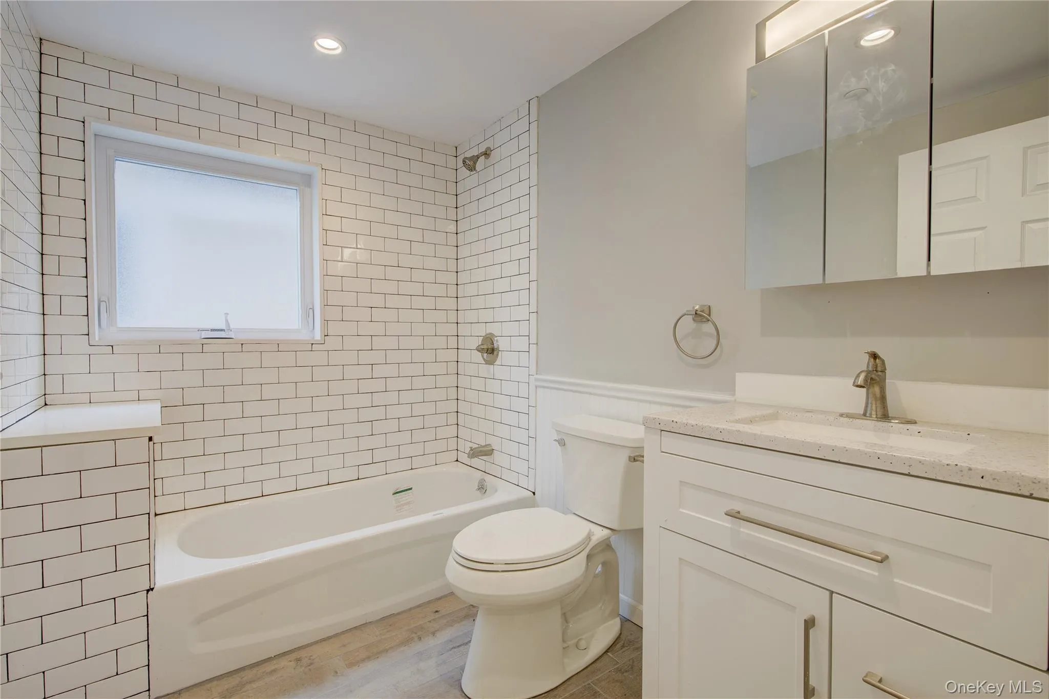 Bathroom featuring vanity, bathtub / shower combination, wainscoting, wood finished floors, and recessed lighting Bathroom featuring vanity, bathtub / shower combination, wainscoting, wood finished floors, and recessed lighting