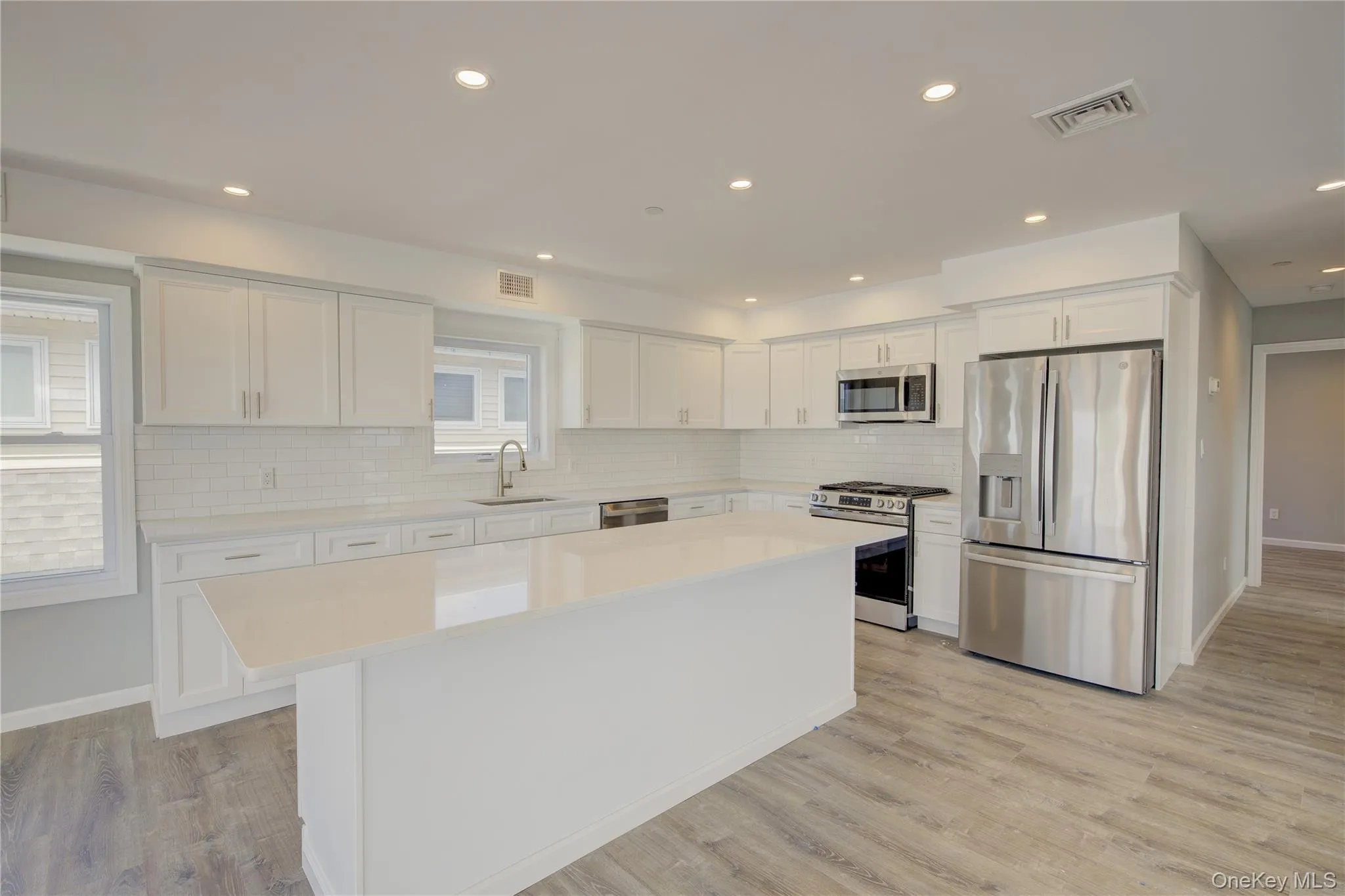 Kitchen featuring stainless steel appliances, white cabinets, a kitchen island, tasteful backsplash, and light countertops Kitchen featuring stainless steel appliances, white cabinets, a kitchen island, tasteful backsplash, and light countertops