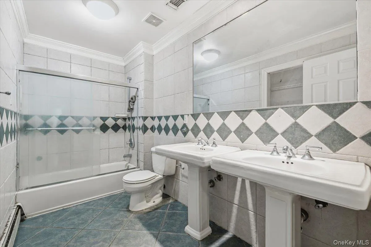2nd floor Main Bathroom featuring tile walls, crown molding, enclosed tub / shower combo, dark tile patterned flooring, and a baseboard heating unit 2nd floor Main Bathroom featuring tile walls, crown molding, enclosed tub / shower combo, dark tile patterned flooring, and a baseboard heating unit