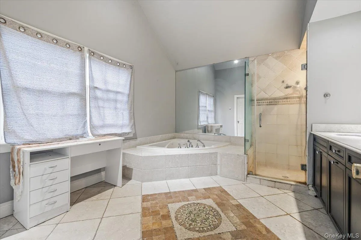 Bathroom with a bath, a shower stall, light tile patterned flooring, lofted ceiling, and vanity Bathroom with a bath, a shower stall, light tile patterned flooring, lofted ceiling, and vanity