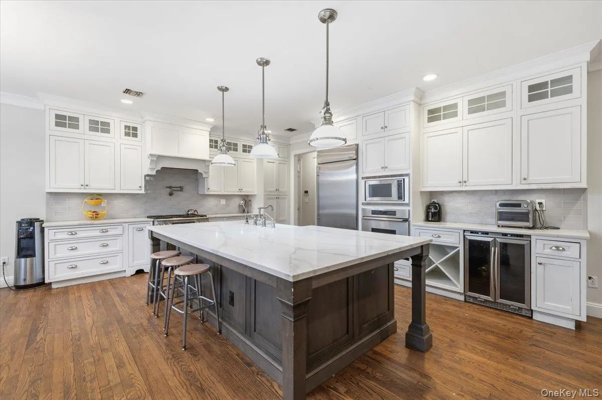 Kitchen with glass insert cabinets, kitchen ornamental molding, wine cooler, a kitchen bar, and white cabinetry Kitchen with glass insert cabinets, kitchen ornamental molding, wine cooler, a kitchen bar, and white cabinetry