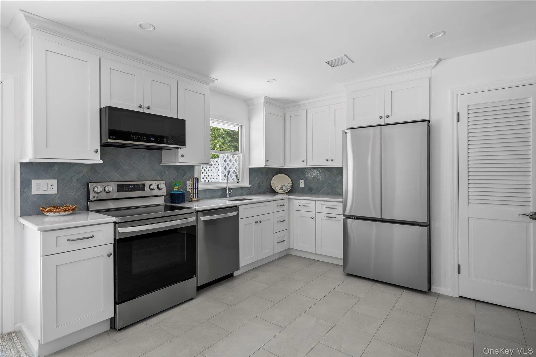 Kitchen with appliances with stainless steel finishes, white cabinets, tasteful backsplash, light tile patterned floors, and recessed lighting Kitchen with appliances with stainless steel finishes, white cabinets, tasteful backsplash, light tile patterned floors, and recessed lighting
