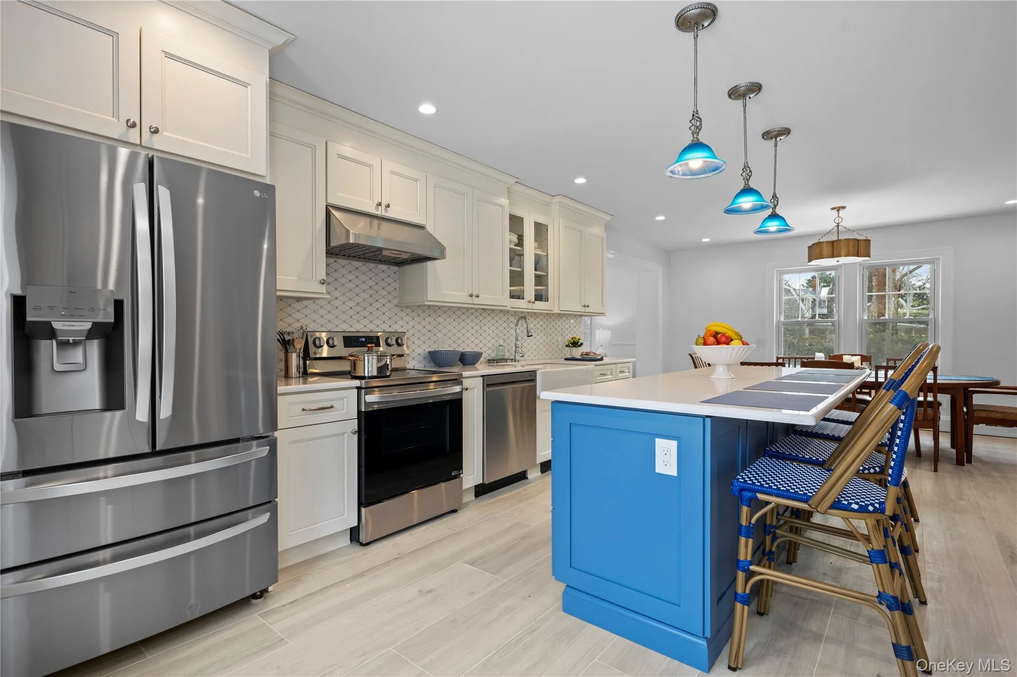 Kitchen with appliances with stainless steel finishes, decorative light fixtures, glass insert cabinets, under cabinet range hood, and a breakfast bar area Kitchen with appliances with stainless steel finishes, decorative light fixtures, glass insert cabinets, under cabinet range hood, and a breakfast bar area
